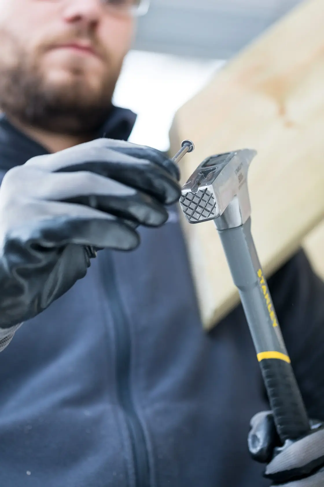 Photo of STANLEY STHT0-51312 steel claw hammer held by a gloved hand, positioning a nail on a wooden board.