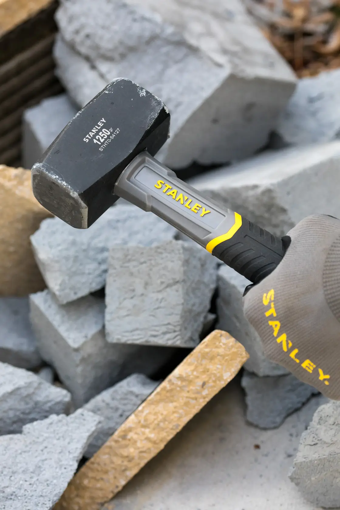 Photo of STANLEY STHT0-54127 mini sledge hammer with gray and yellow handle breaking concrete blocks.