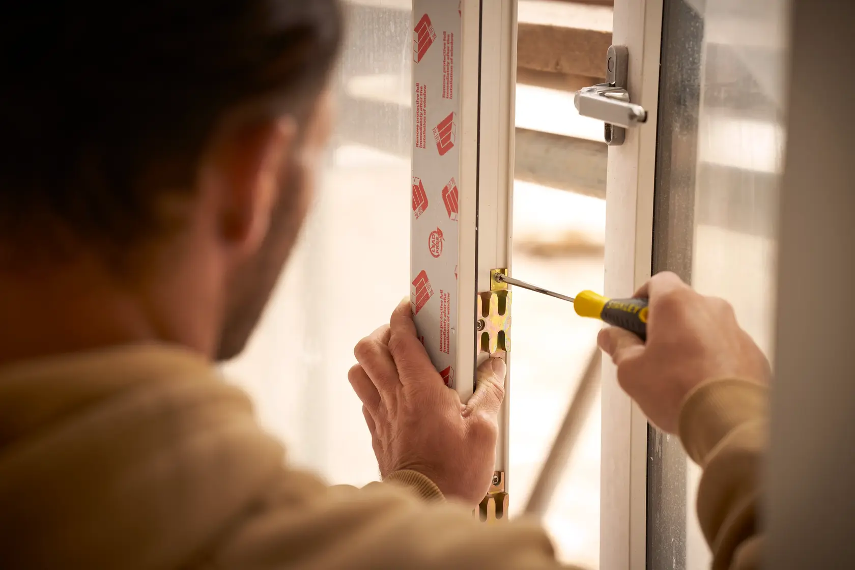 STANLEY STHT0-60335 screwdriver used to tighten a screw on a window latch during installation.