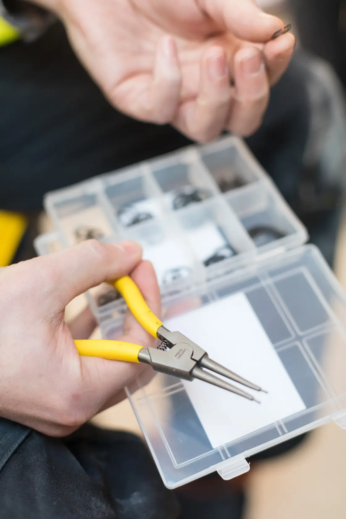 STANLEY STHT0-75412 pliers with yellow handles held beside a divided case of small hardware, close-up view.