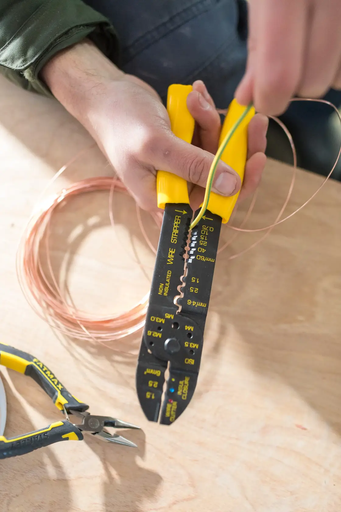 STANLEY STHT0-75414 wire stripper with yellow handle held over copper wire on wooden table, close-up view.