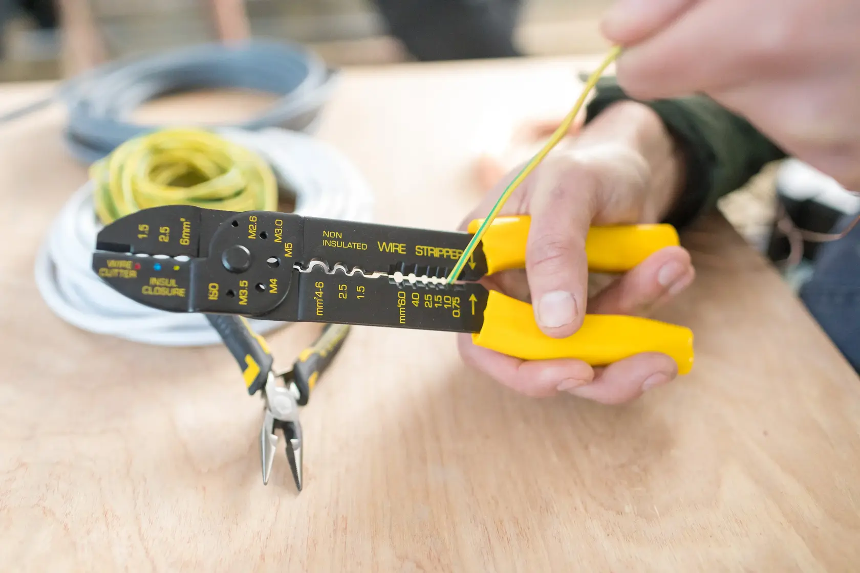 STANLEY STHT0-75414 wire stripper with yellow handles held by hand, stripping yellow wire on a workbench.