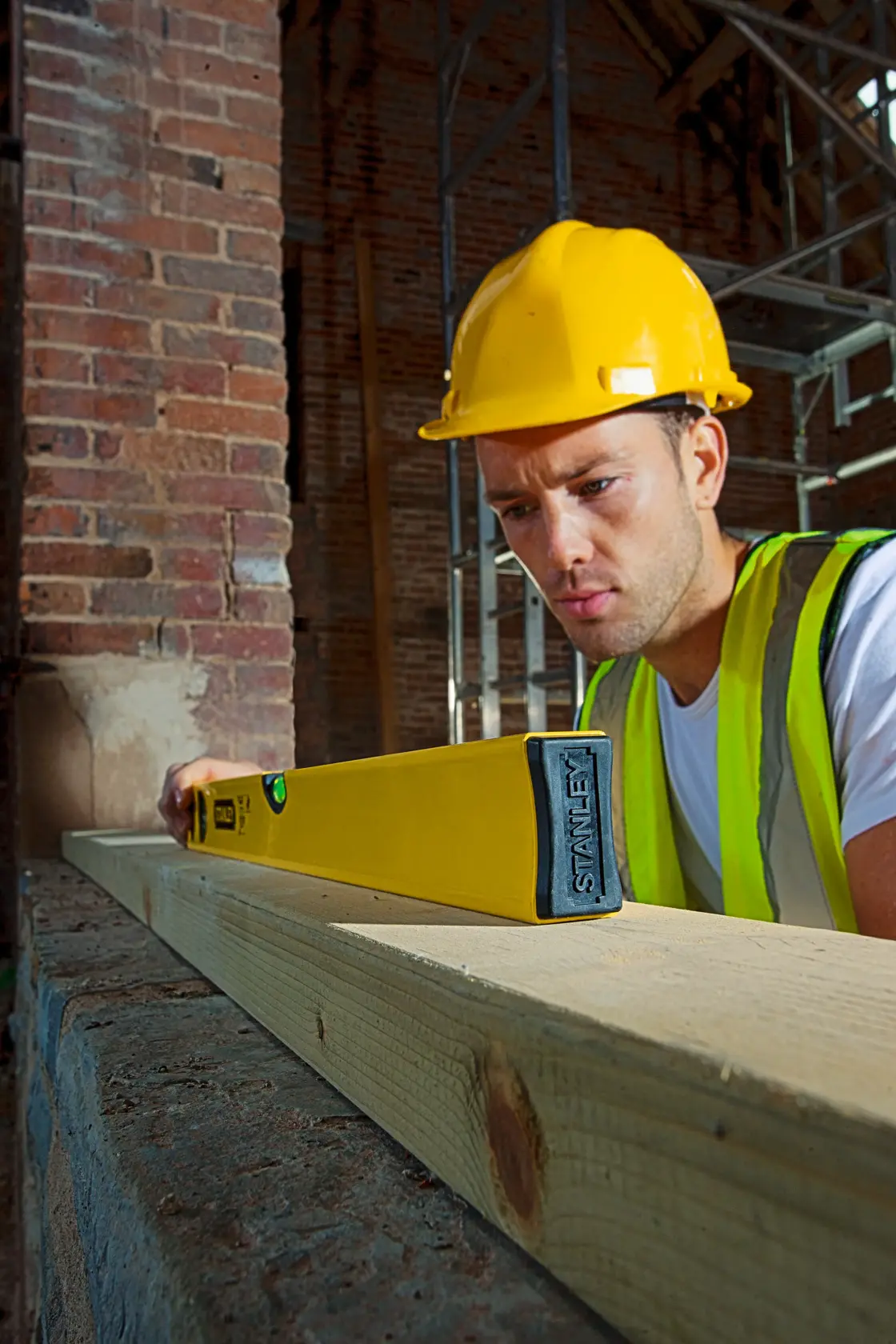 Stanley STHT1-43102-IU2-M yellow level tool on wood plank at construction site, front angle, photography.
