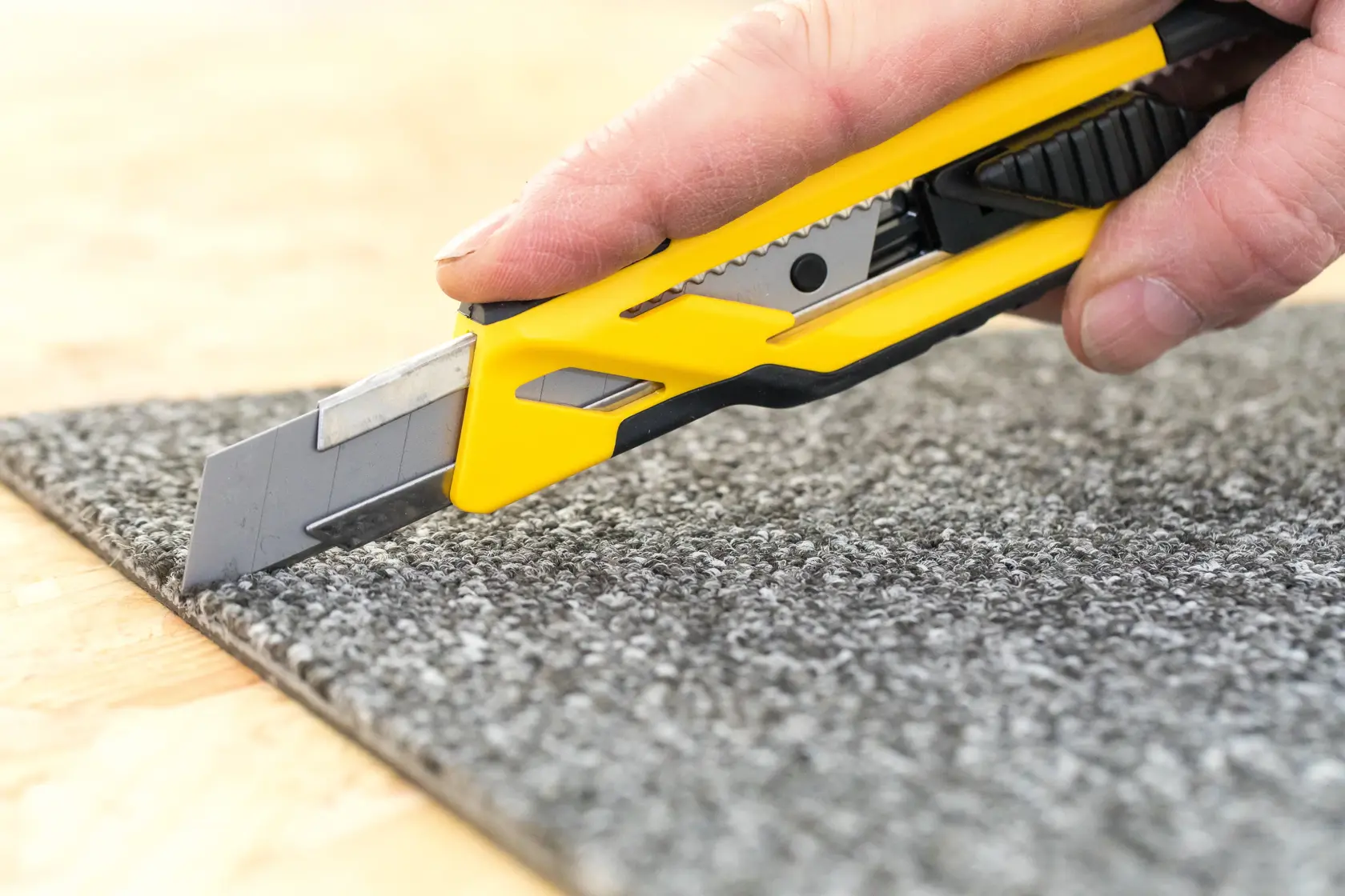 STANLEY STHT10266-0 Universalmesser mit gelb-schwarzem Griff schneidet grauen Teppich aus nächster Nähe.