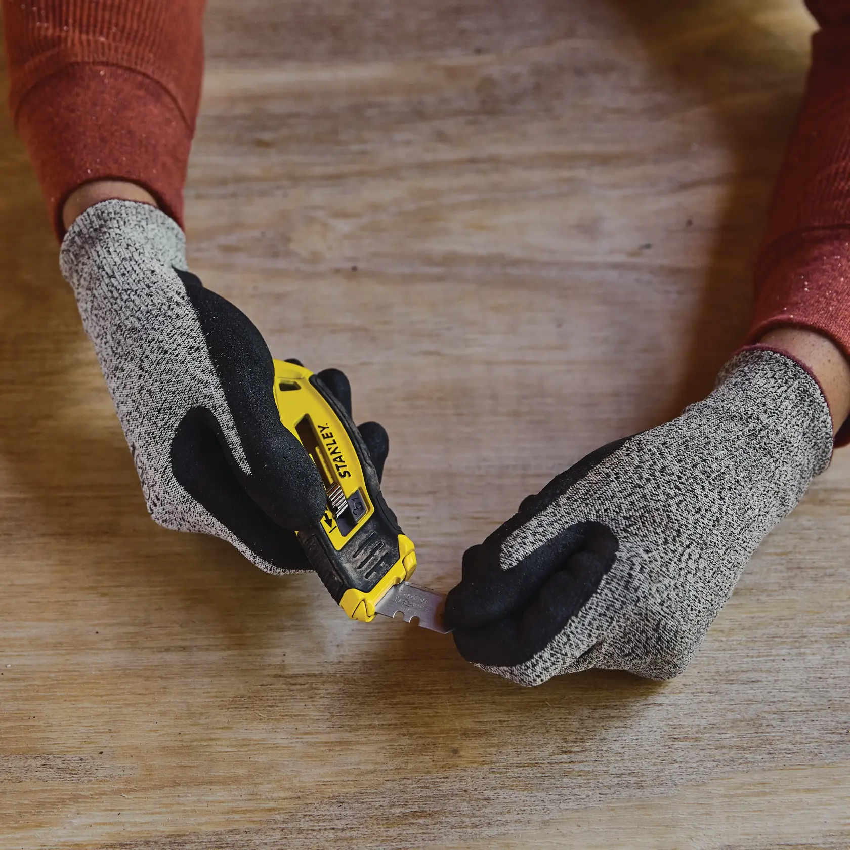 Foto des STANLEY STHT10432-0 Universalmessers, gehalten mit Handschuhen, Klinge ausgefahren, auf Holzoberfläche.