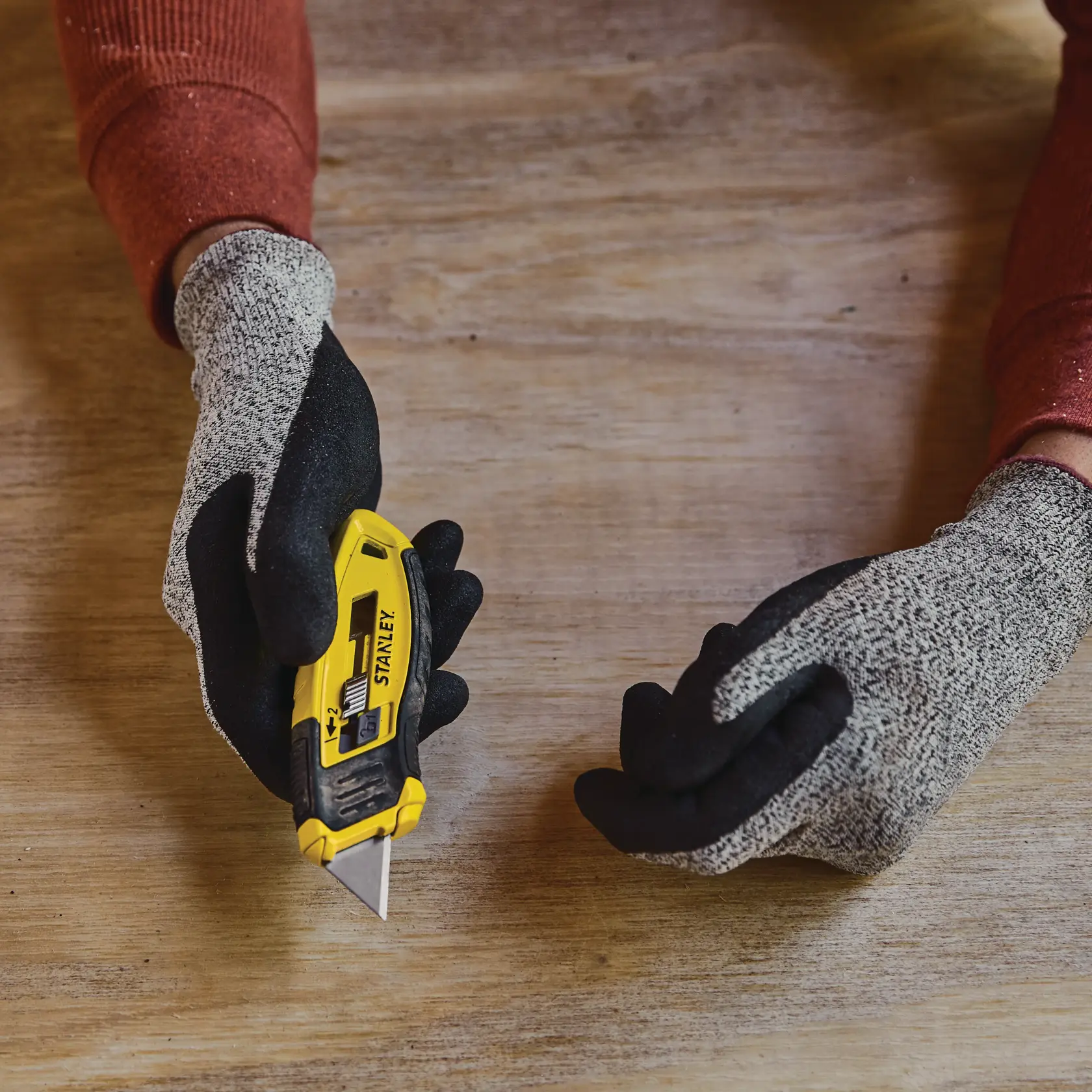 Foto vom STANLEY STHT10432-0 Universalmesser in behandschuhter Hand auf Holzoberfläche.
