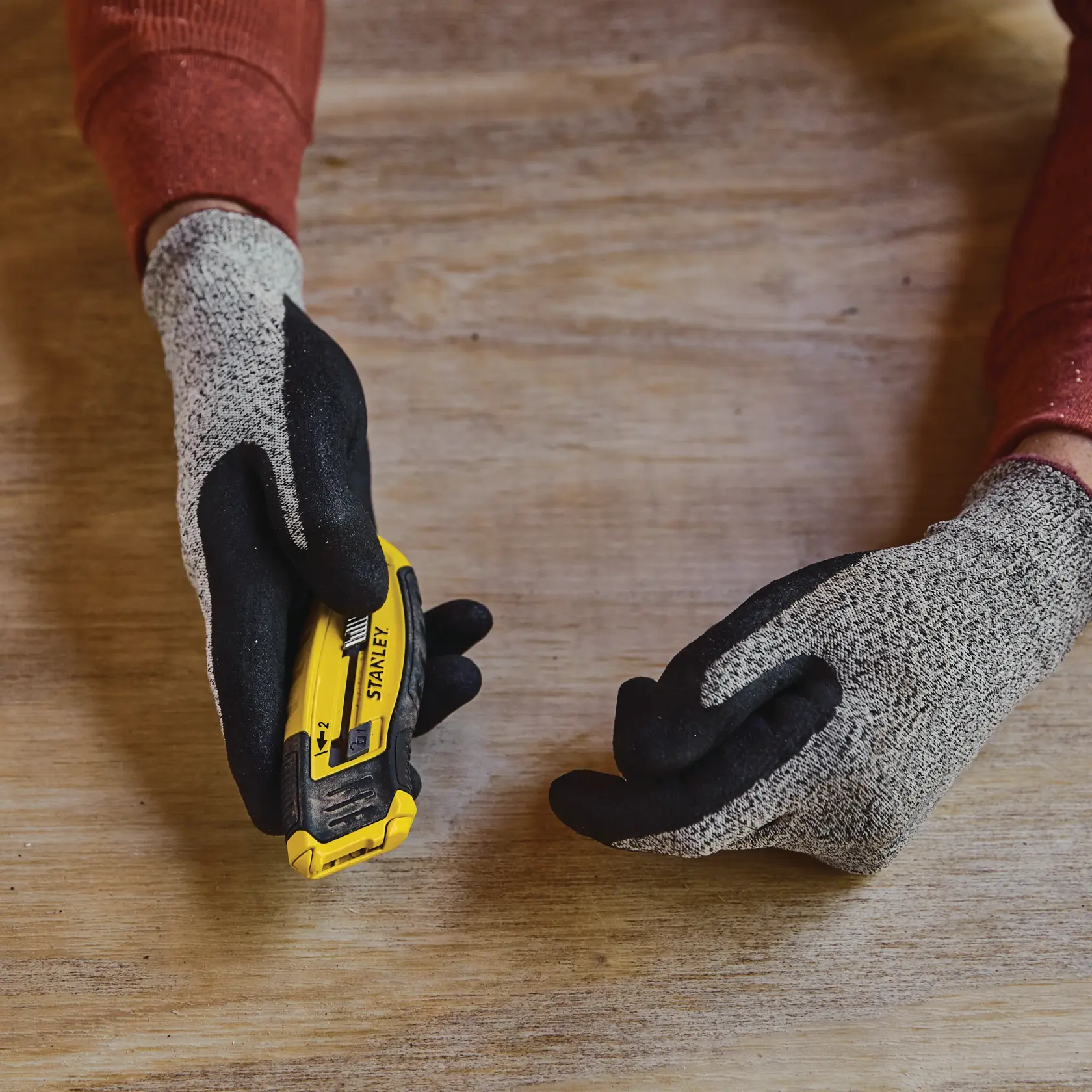 Foto des STANLEY STHT10432-0 Universalmessers in behandschuhter Hand auf Holzoberfläche.