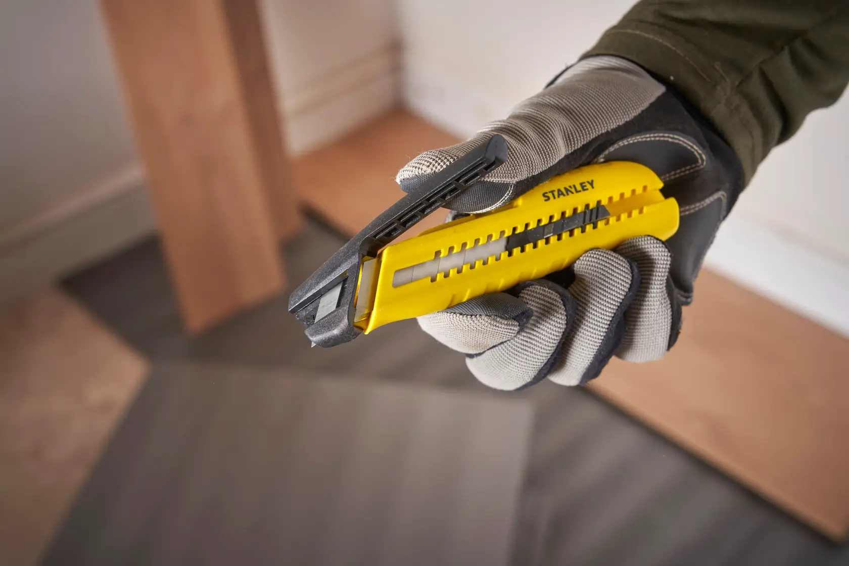 Photo of STANLEY utility knife, yellow and black, handheld, SKUs STHT10489, STHT10489-0, used in flooring work.