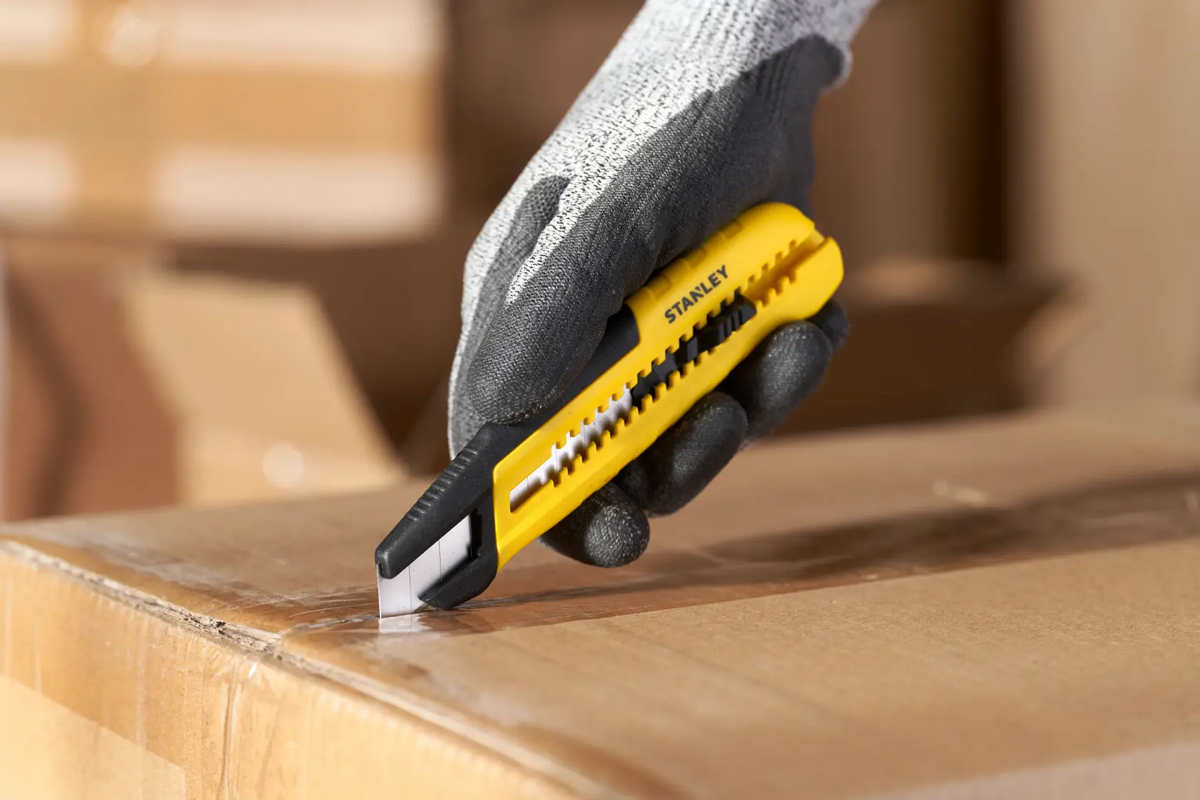 Photo of STANLEY STHT10489, STHT10489-0 yellow utility knife cutting box, held by gloved hand, photography category.