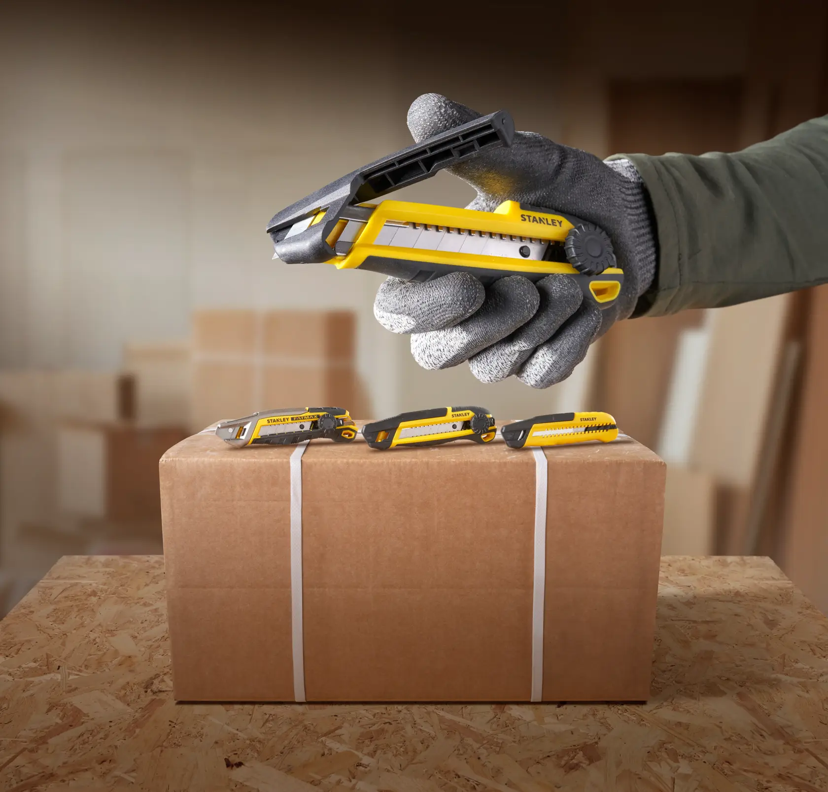 Photo of STANLEY STHT10500-0 utility knife, yellow and black, used for cutting box tape, hand in work glove.
