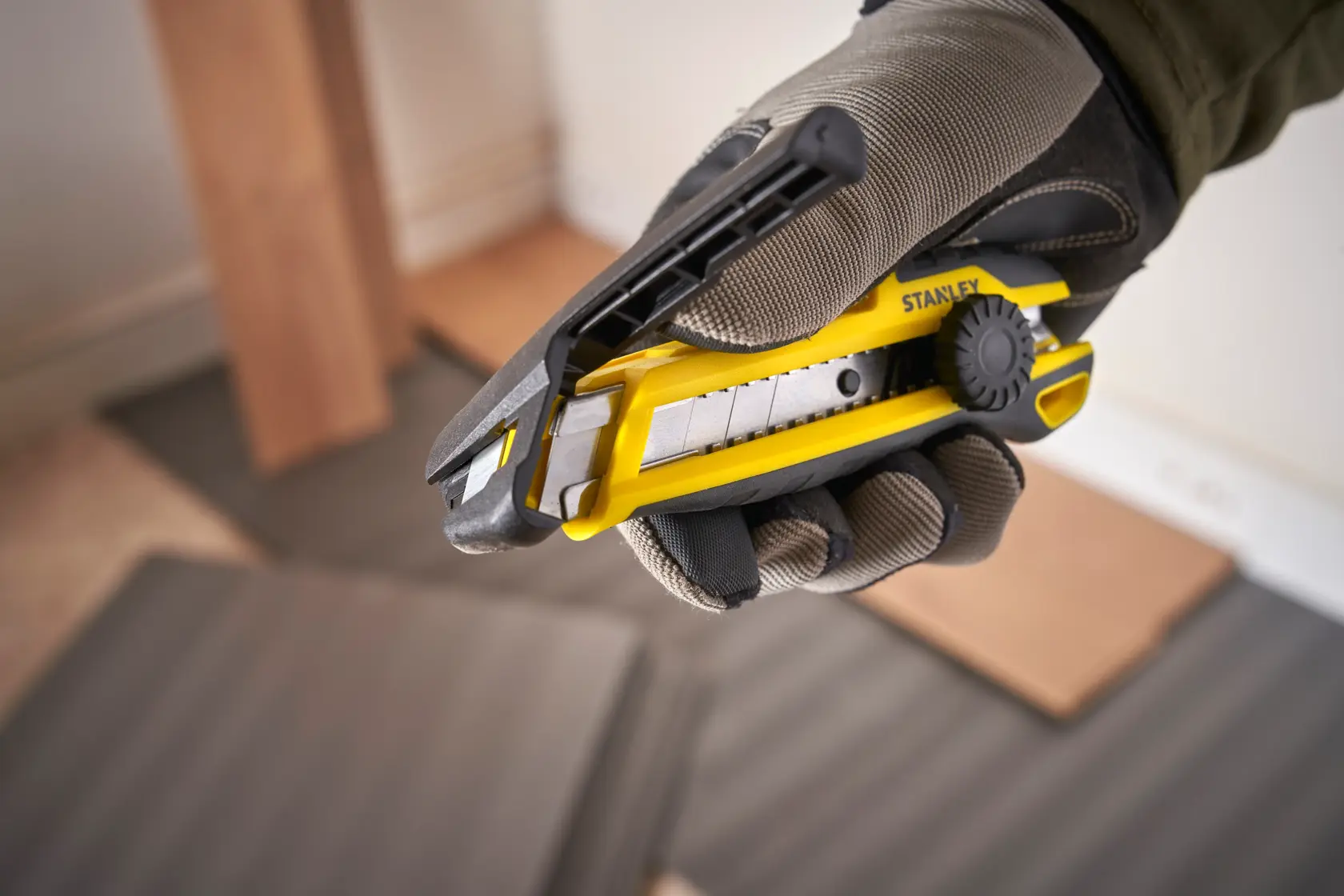 Photo of STANLEY STHT10500-0 utility knife with segmented blade, yellow and black, held in gloved hand.