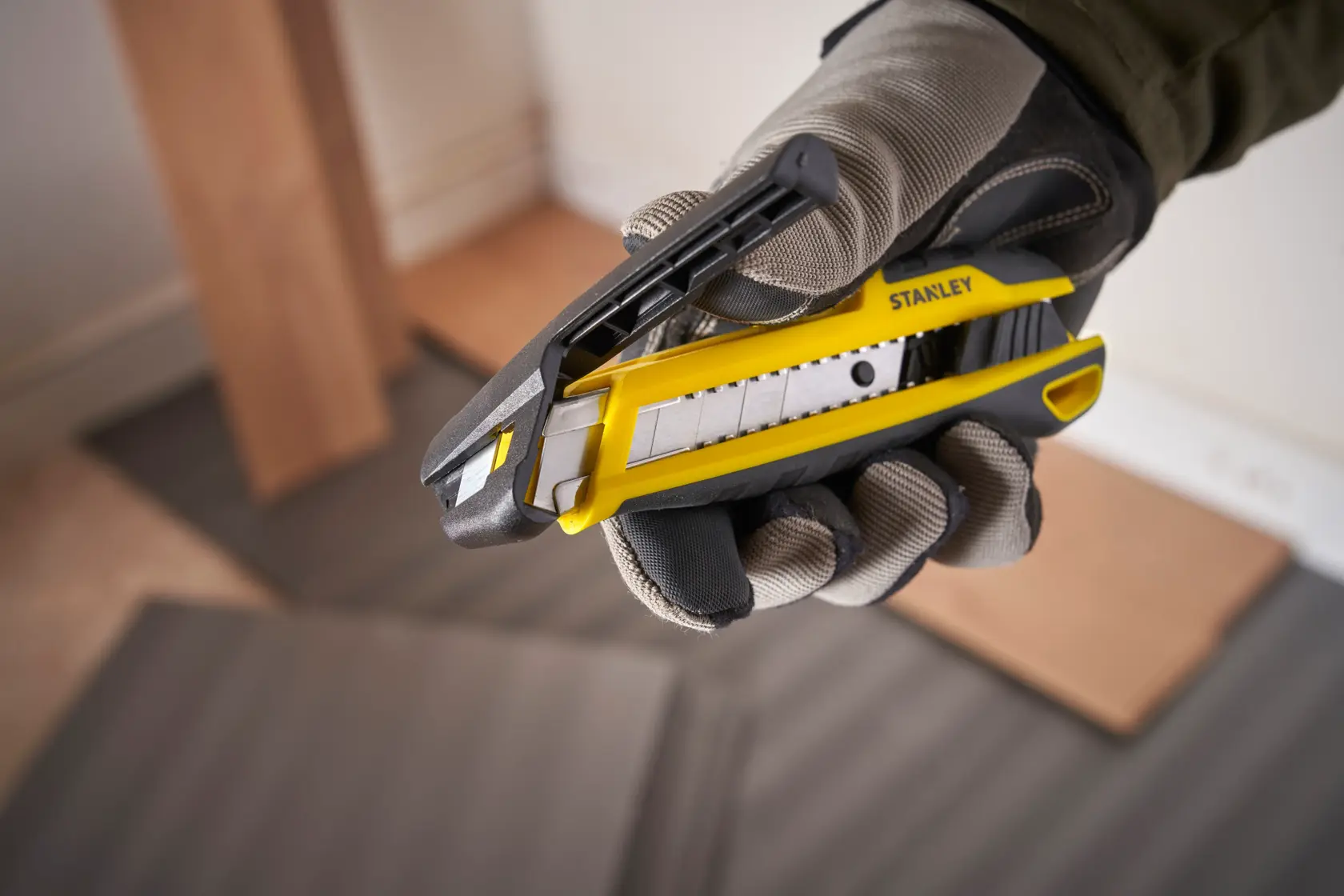 Photo of STANLEY STHT10501-0 utility knife, yellow and black, held in gloved hand, product close-up.