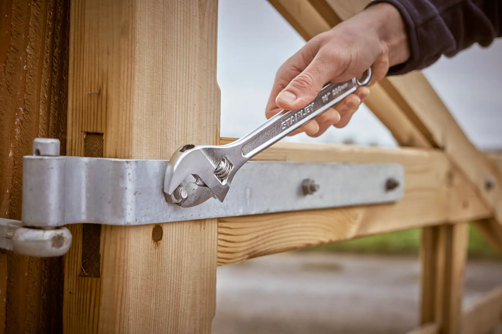 Photography of STANLEY STHT13121-0 adjustable wrench tightening a metal hinge on a wooden gate.