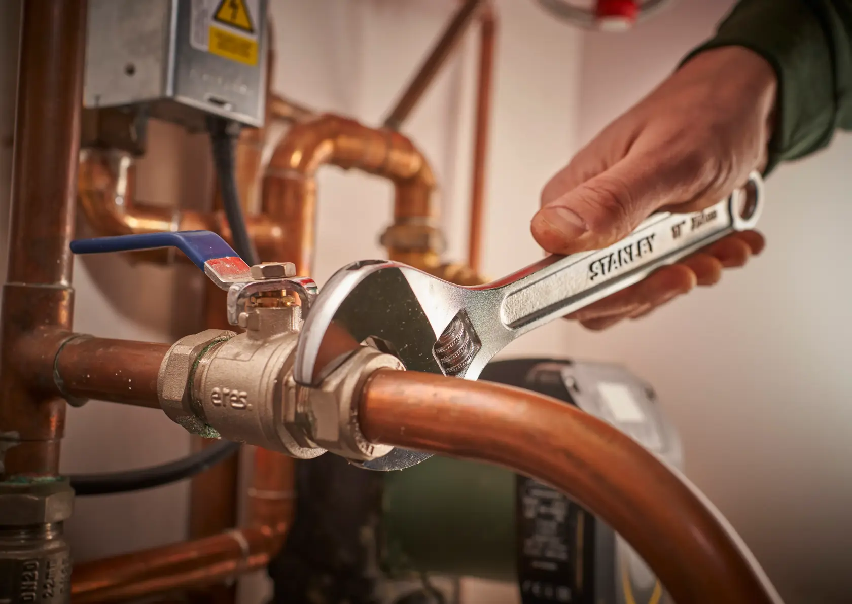 Photo of STANLEY STHT13121-0 adjustable wrench tightening a pipe fitting in a plumbing setup.