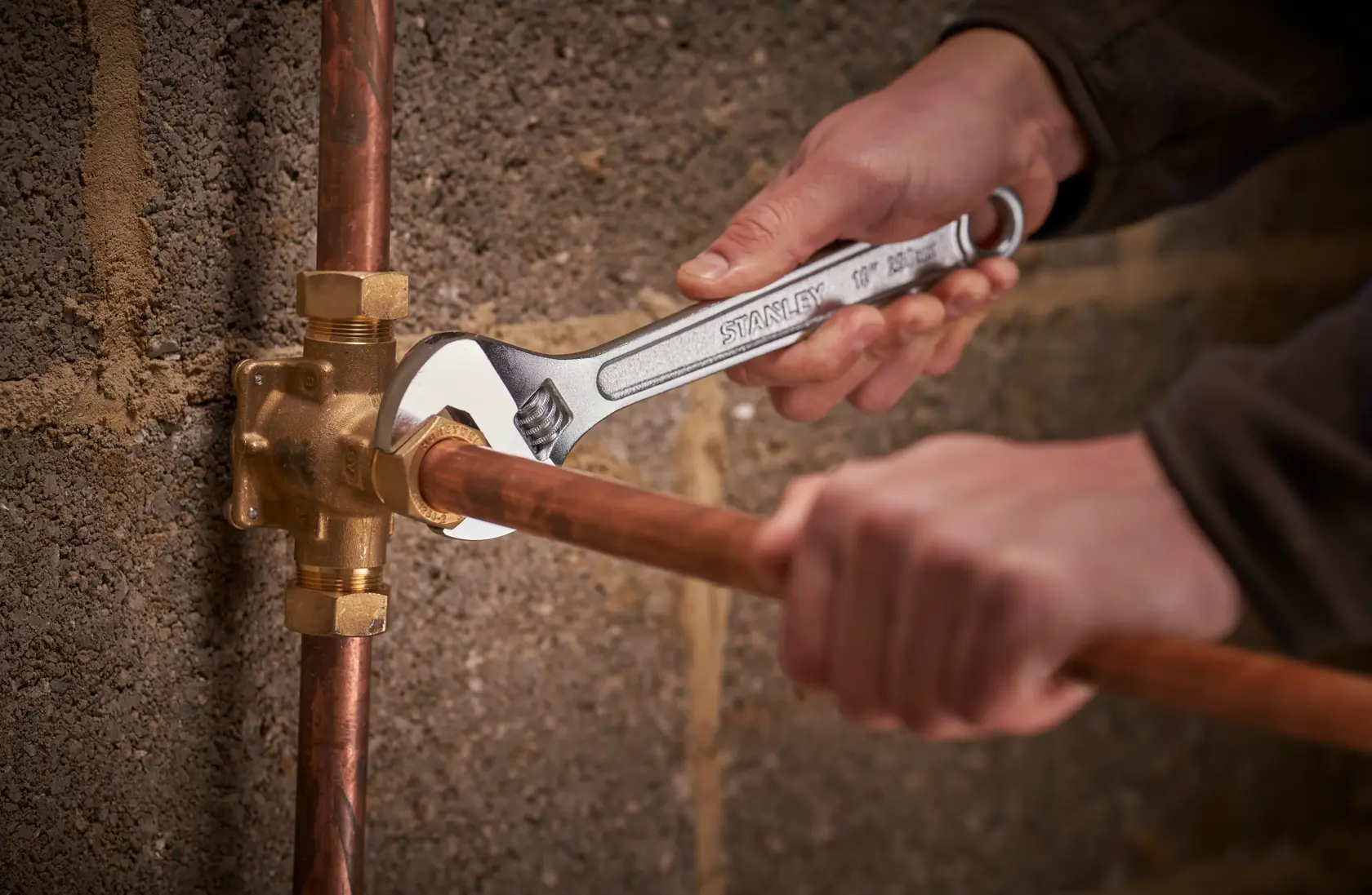 Photo of STANLEY STHT13123-0 adjustable wrench used on copper pipe near wall, tool held by hand.