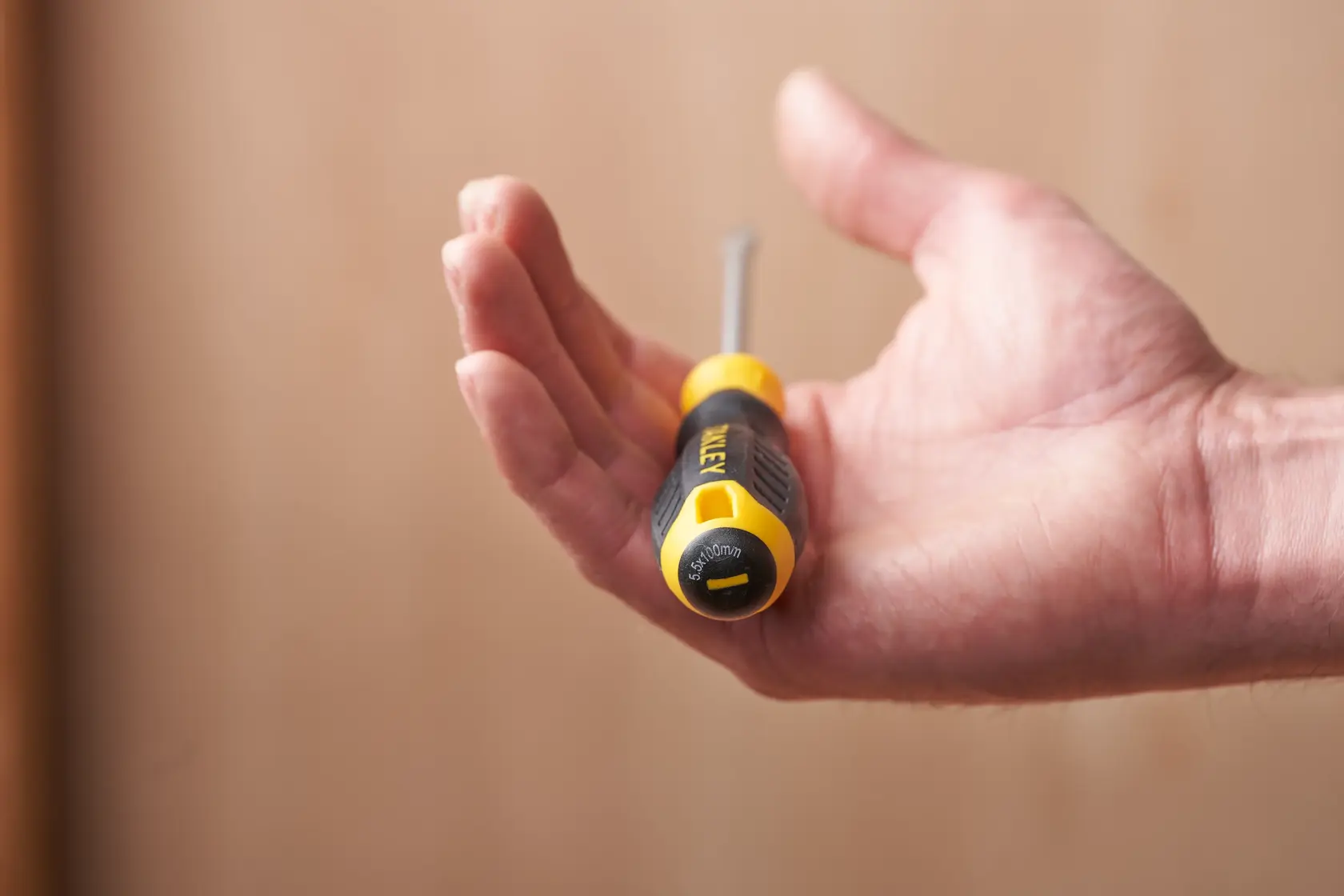STANLEY STHT16146-0 screwdriver with yellow and black handle held in hand, side angle, photography product.