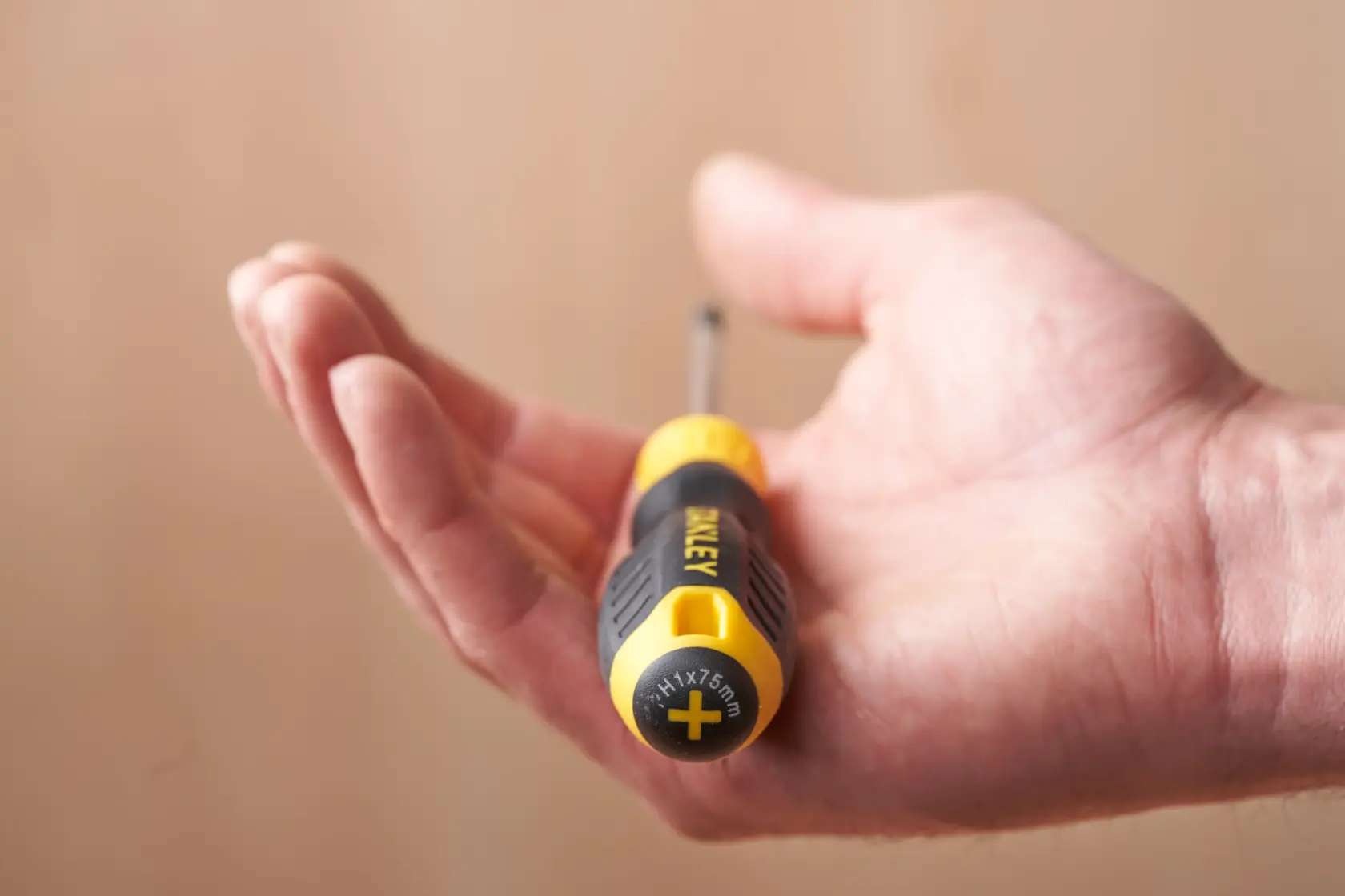 Stanley STHT16155-0 screwdriver with black and yellow handle held in hand, close-up photography.