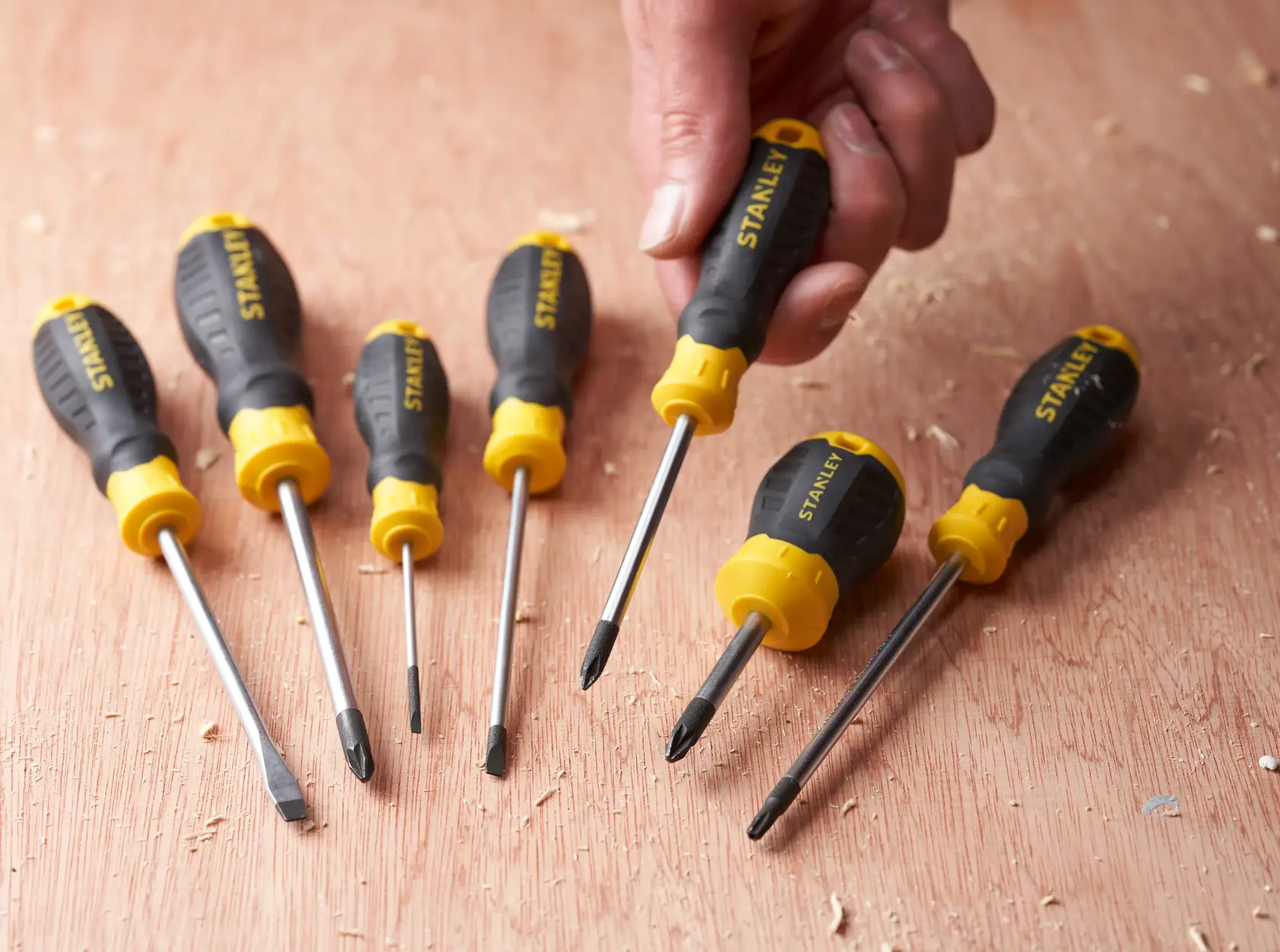 STANLEY STHT16155-0 screwdriver set with black and yellow handles on wooden surface, one held in hand.