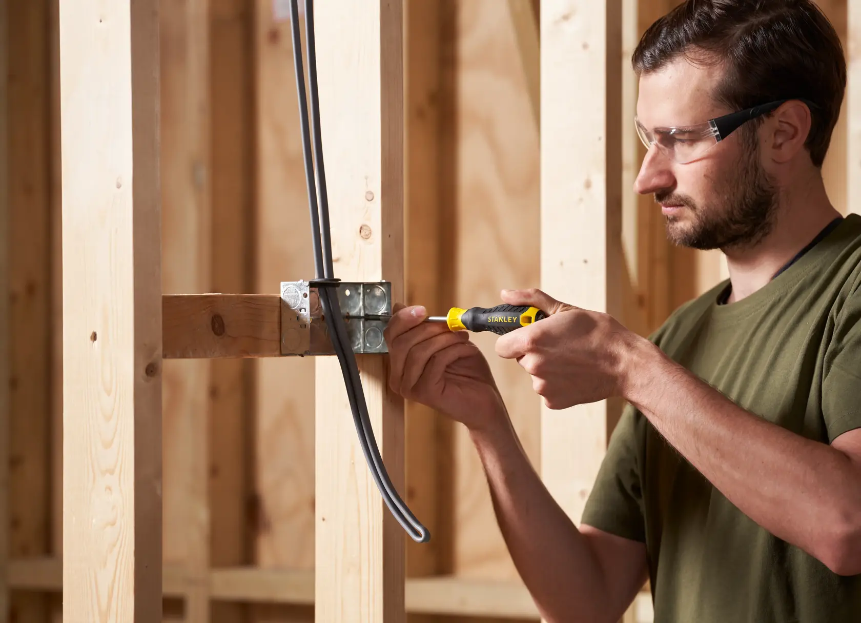 Photo of person using STANLEY STHT16163-0 screwdriver on an electrical box, wooden frame background.