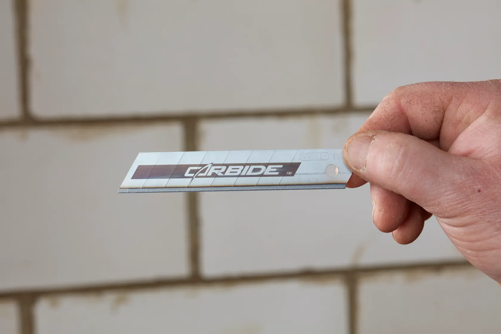 STANLEY STHT2-11818 Cutterklinge, silber mit carbide-Aufdruck, von Hand vor gefliester Wand gehalten.