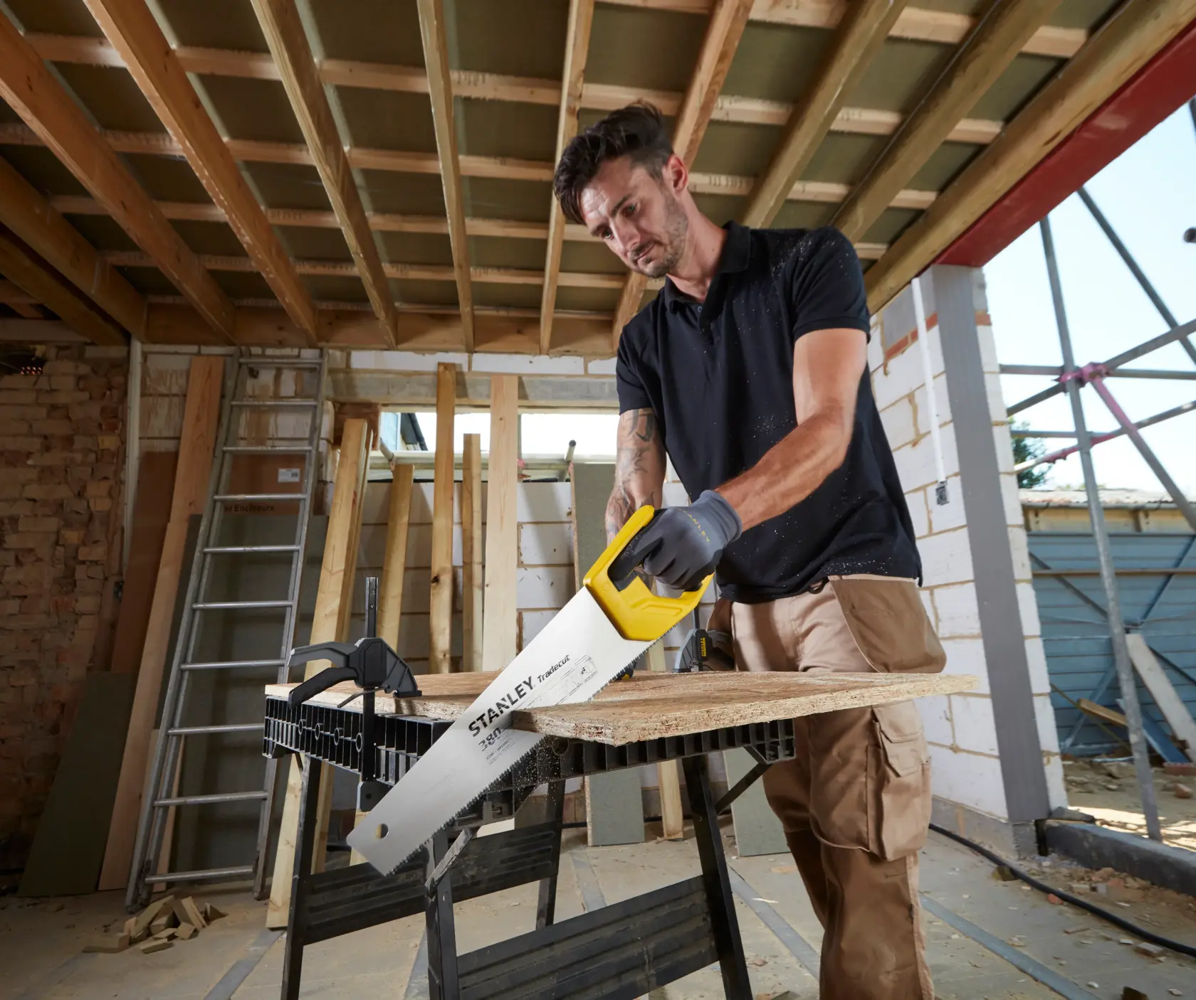 STANLEY STHT20348-1 hand saw with yellow handle cutting wood plank on construction site.