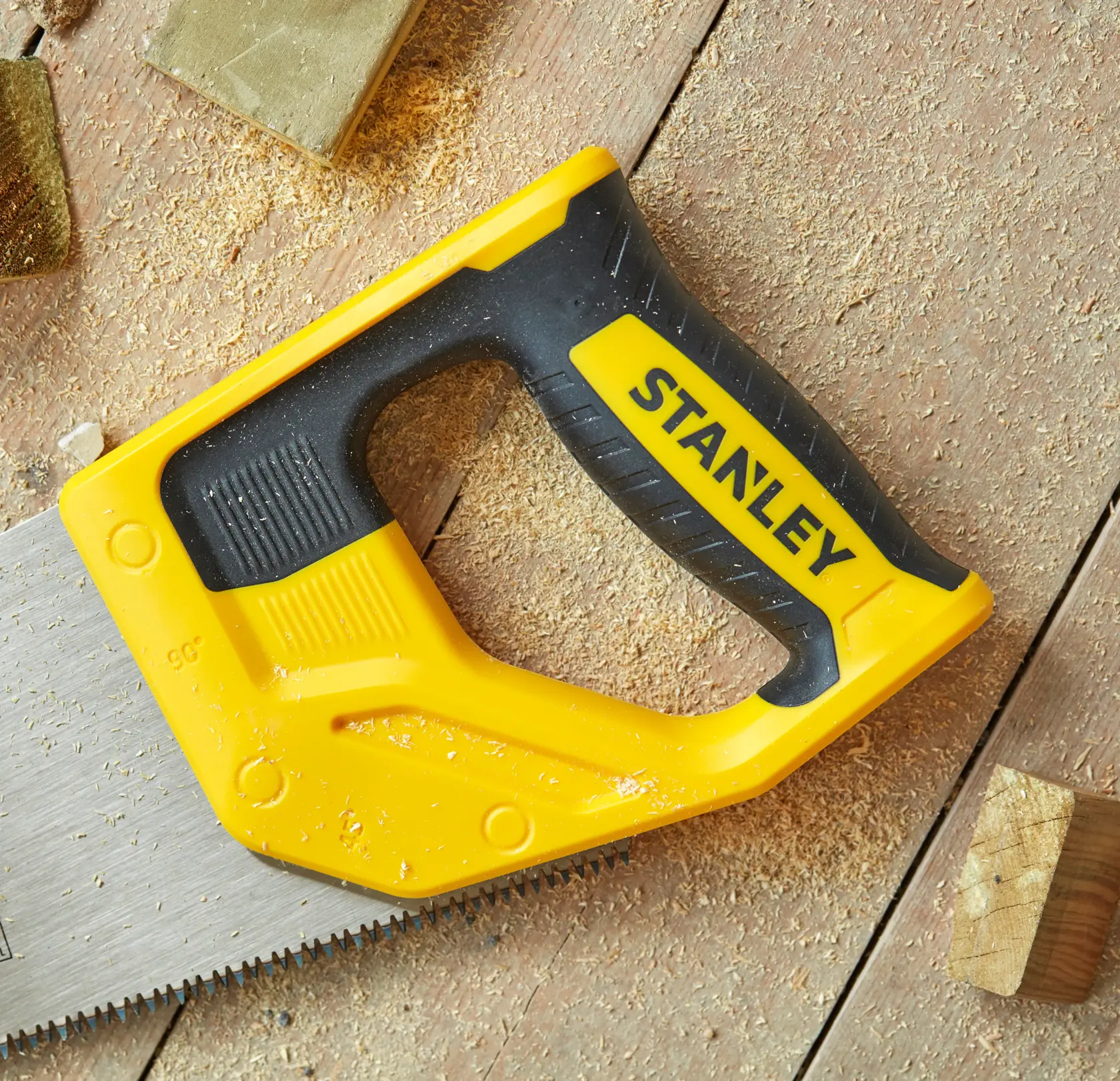 Photo of STANLEY STHT20348-1 hand saw with yellow and black handle on wood surface with sawdust.