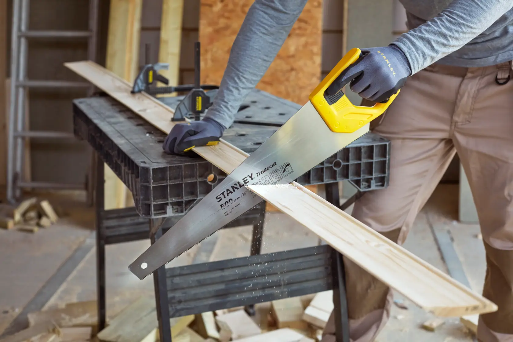 STANLEY STHT20350-1 hand saw with yellow handle cutting wood plank in workshop, photography category.