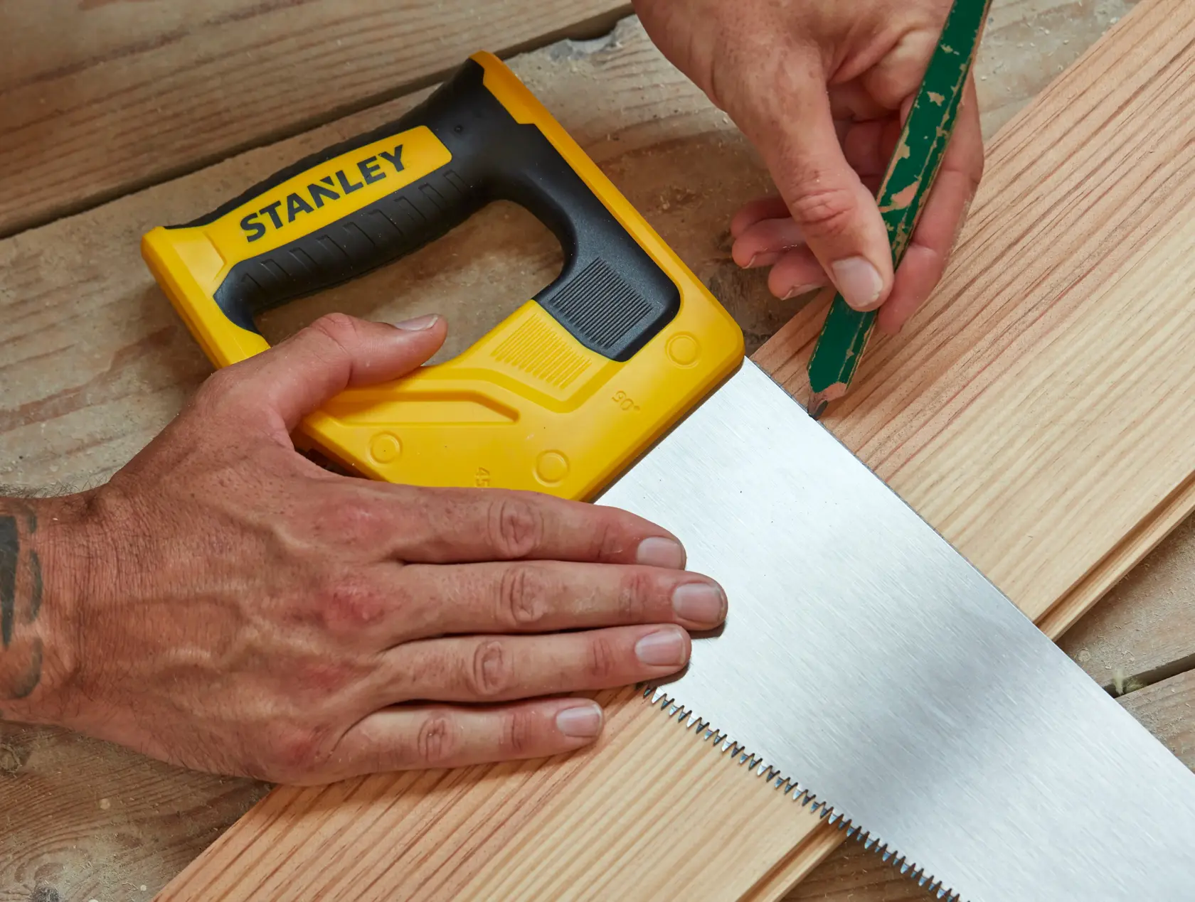 Stanley STHT20350-1 hand saw with yellow and black handle on wood, person marking with pencil.