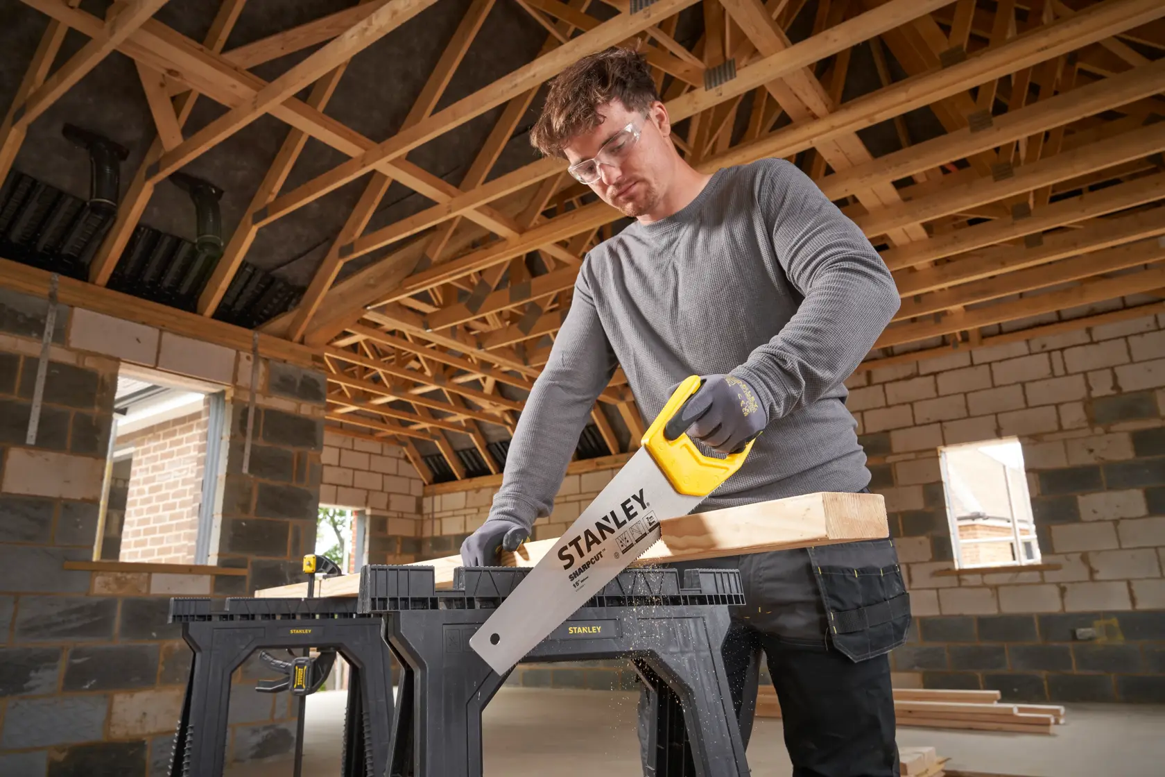 STANLEY STHT20366-1 hand saw cutting wood on saw horse, indoor construction site.