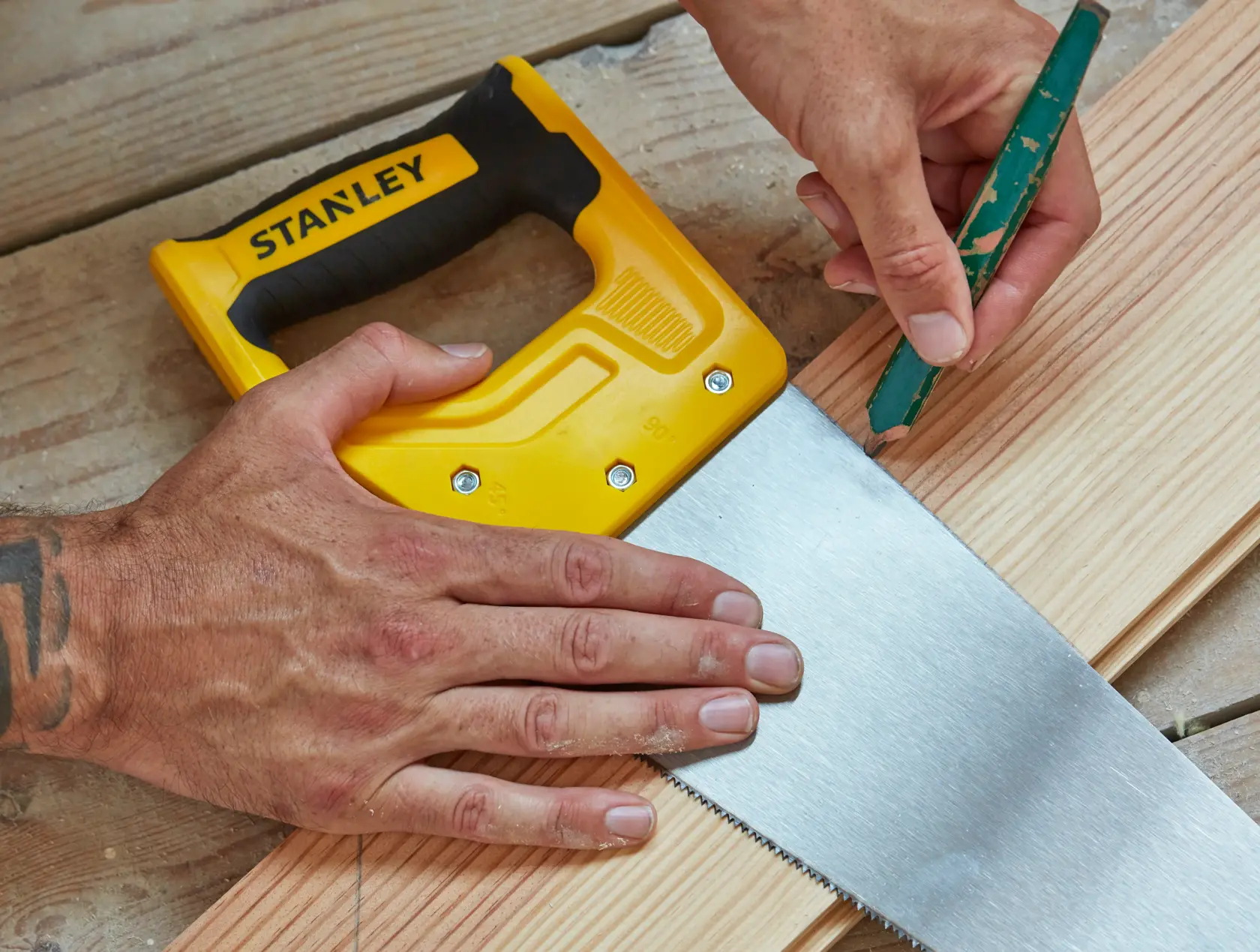 STANLEY STHT20369-1 yellow and black hand saw on wood planks, close-up with hands marking cut line.