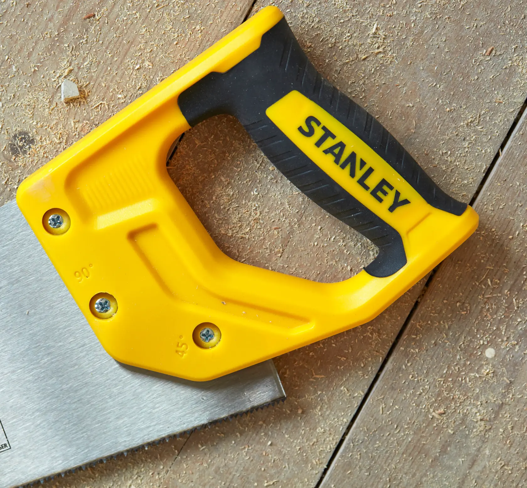 STANLEY STHT20369-1 handsaw with yellow and black handle, photographed on a wooden surface with sawdust.