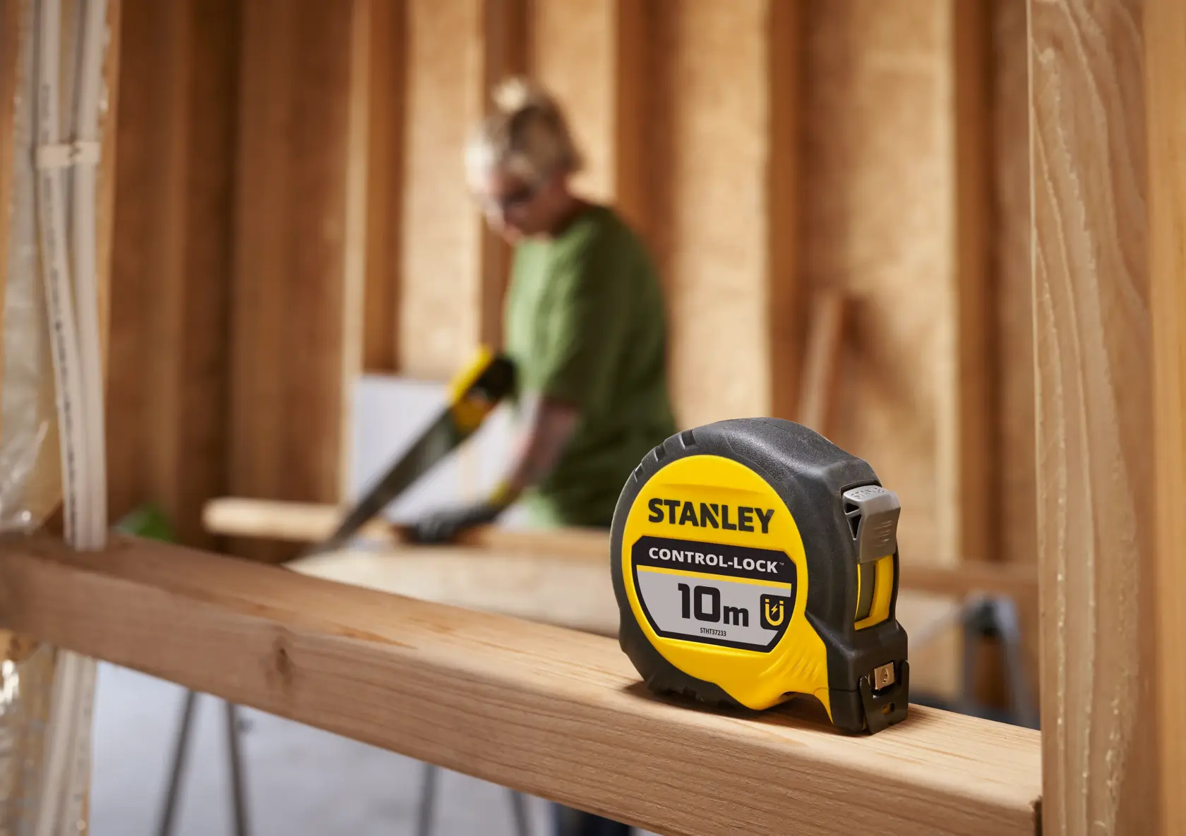 Stanley STHT37233-0 Maßband, 10 m, gelb und schwarz, auf Holzträger mit unscharfem Hintergrund.