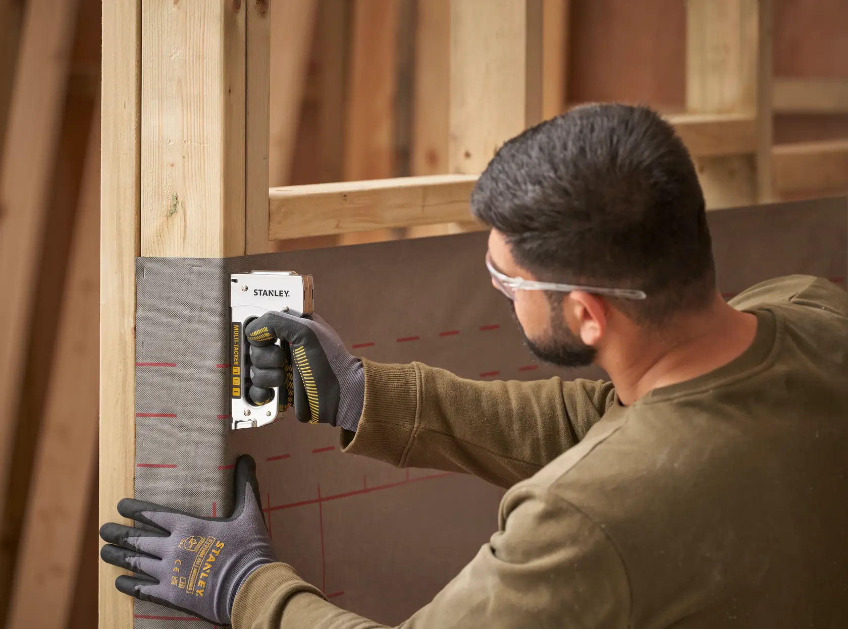 Person using STANLEY STHT6-70410 manual stapler to attach material to wooden frame, side view.