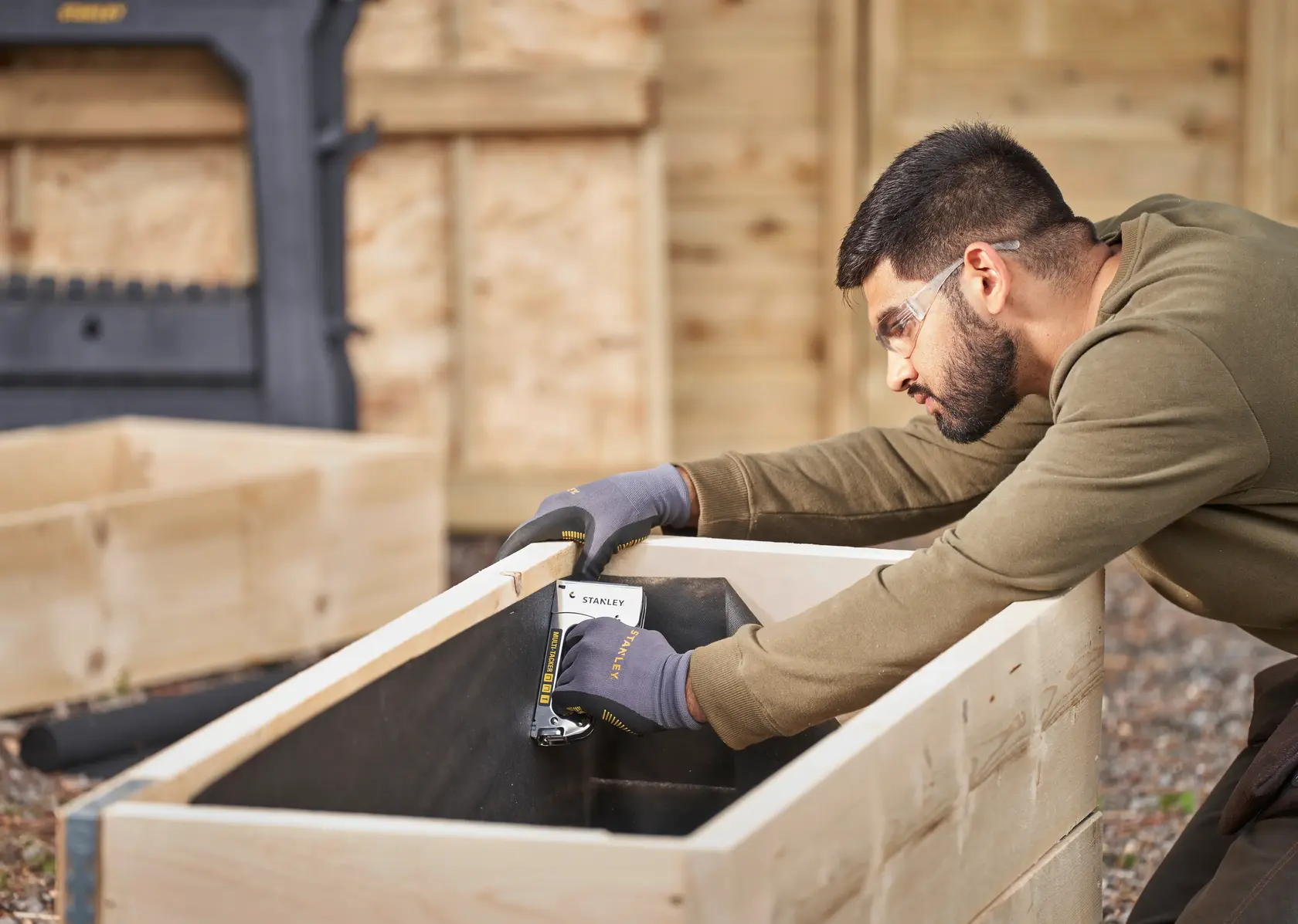 Photo of STANLEY STHT6-70410 stapler used to secure lining inside a wooden planter outdoors.