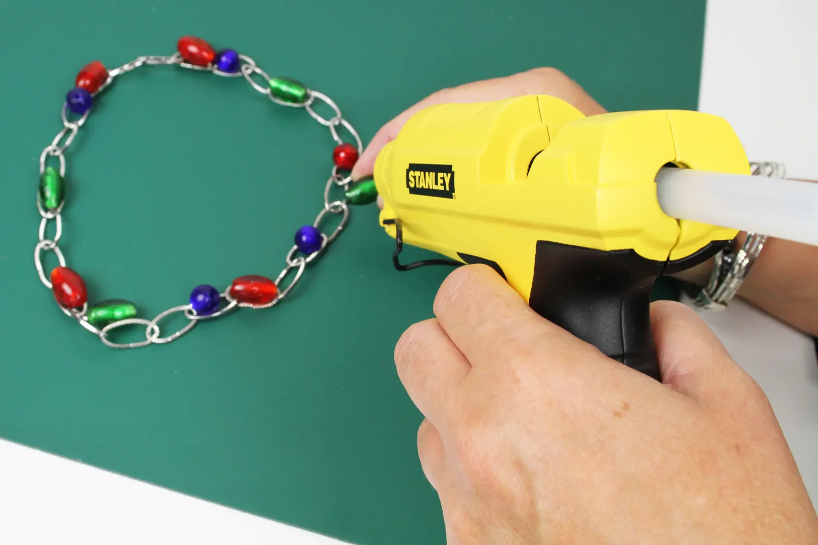 STANLEY STHT6-70417 yellow glue gun used to assemble a colorful beaded chain on a green surface.