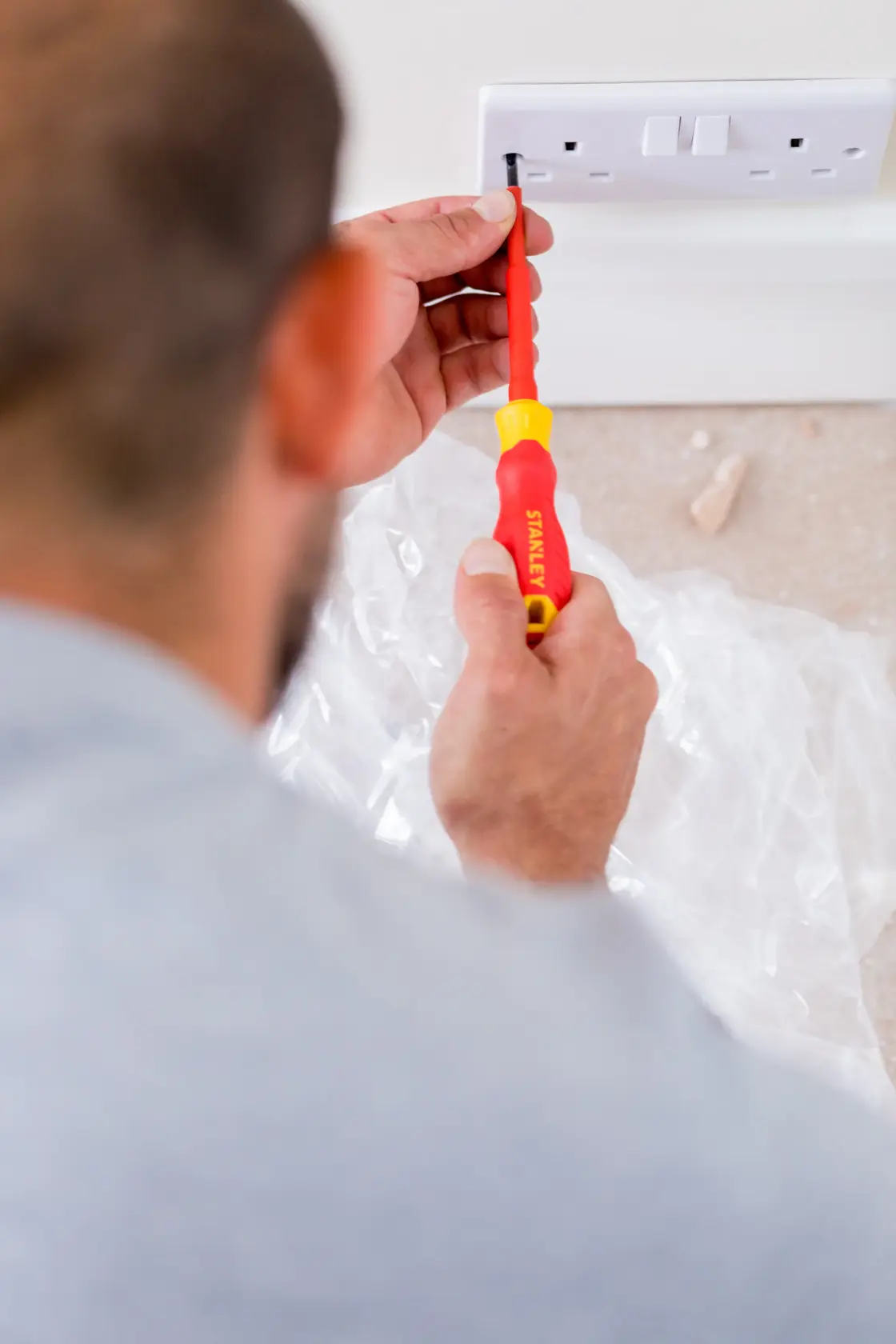 Photo of a person using a STANLEY STHT60032-0 red and yellow screwdriver to install a wall power socket.