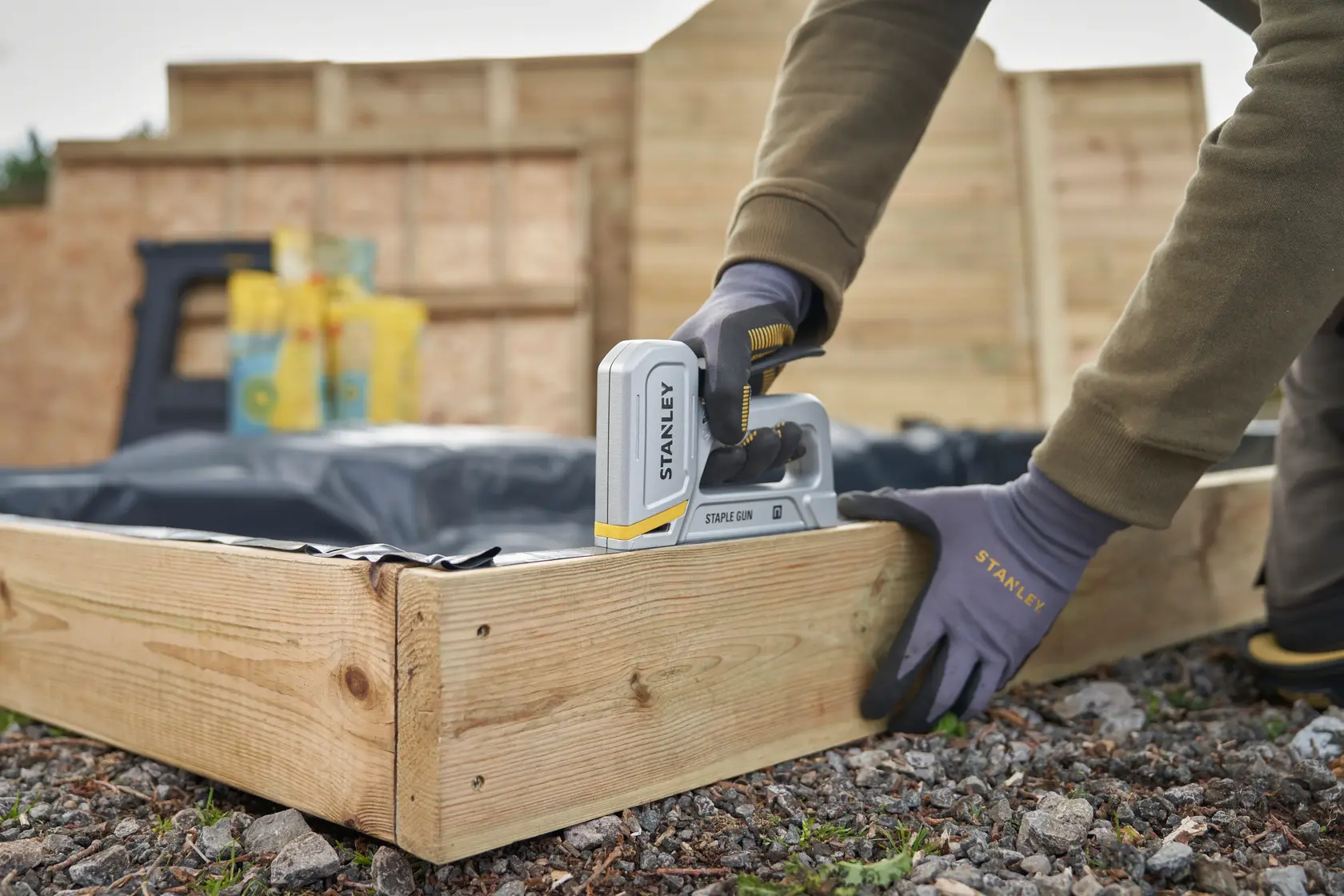Photo of STANLEY STHT70150-0 staple gun in use attaching plastic to wooden garden bed outdoors.