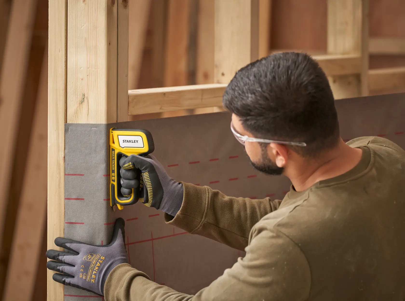 Stanley STHT70440-0 staple gun used to fasten sheet to wooden frame, user wearing gloves and safety glasses.