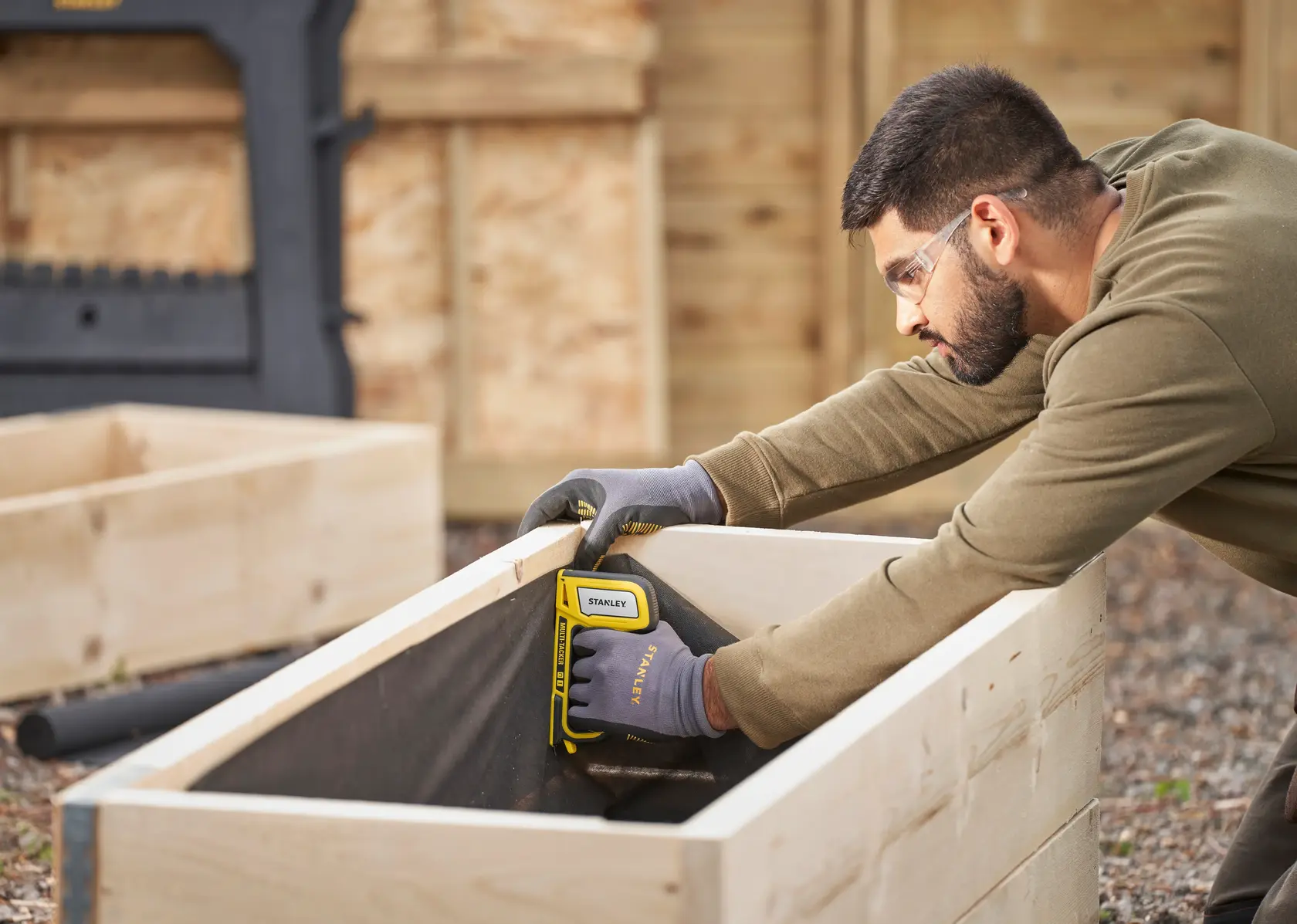 Photo of STANLEY STHT70440-0 stapler in use attaching fabric to wooden planter box outdoors.