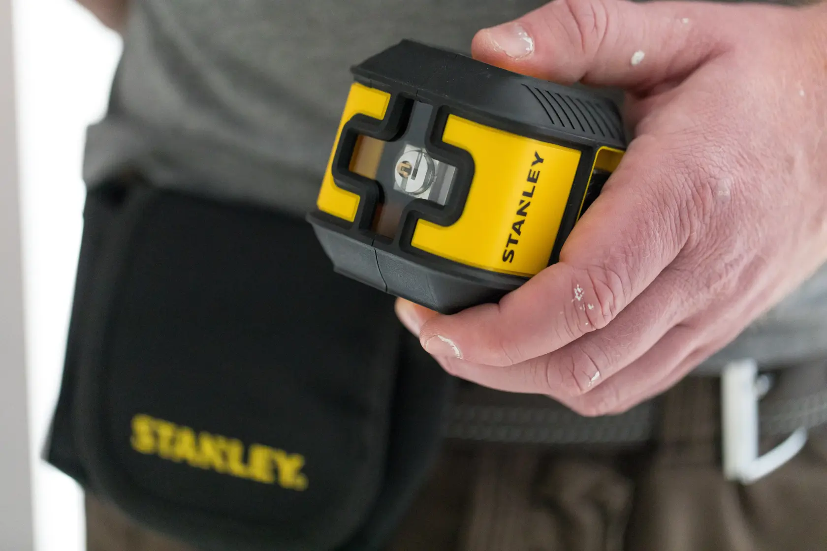 Foto des STANLEY STHT77499-1 Laser-Nivelliergeräts in Gelb und Schwarz, in der Hand gehalten, Werkzeugtasche sichtbar.