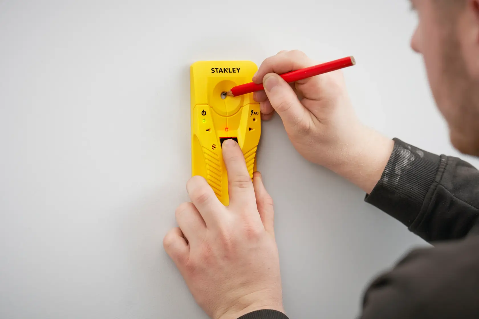 STANLEY STHT77587-0 yellow stud finder held against wall, user marking spot with red pencil.