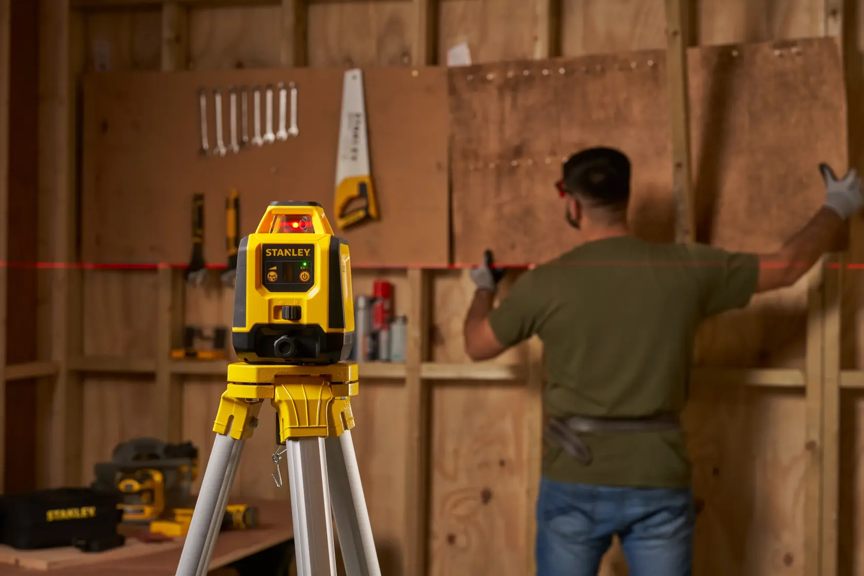 STANLEY STHT77616-0 laser level on tripod projects red line in workshop with person aligning boards.