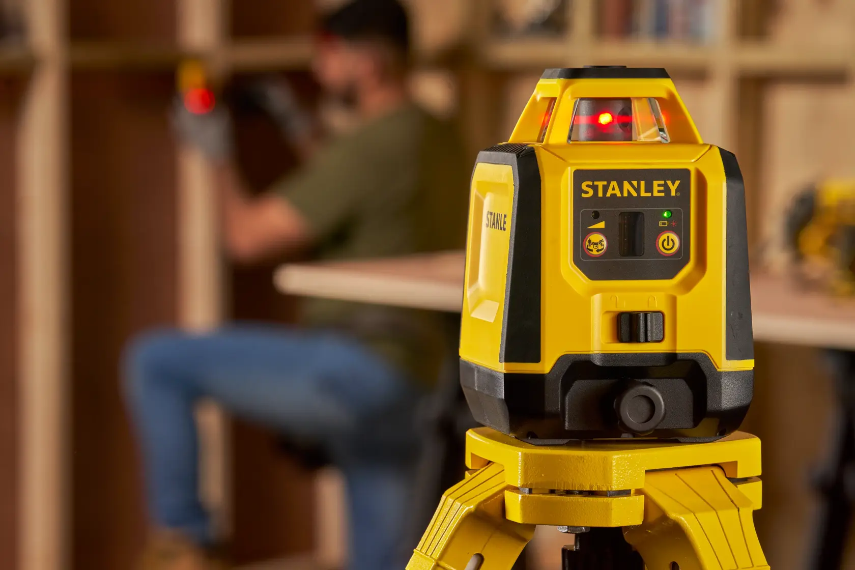 Photo of STANLEY STHT77616-0 laser level on tripod, focused in workshop setting.