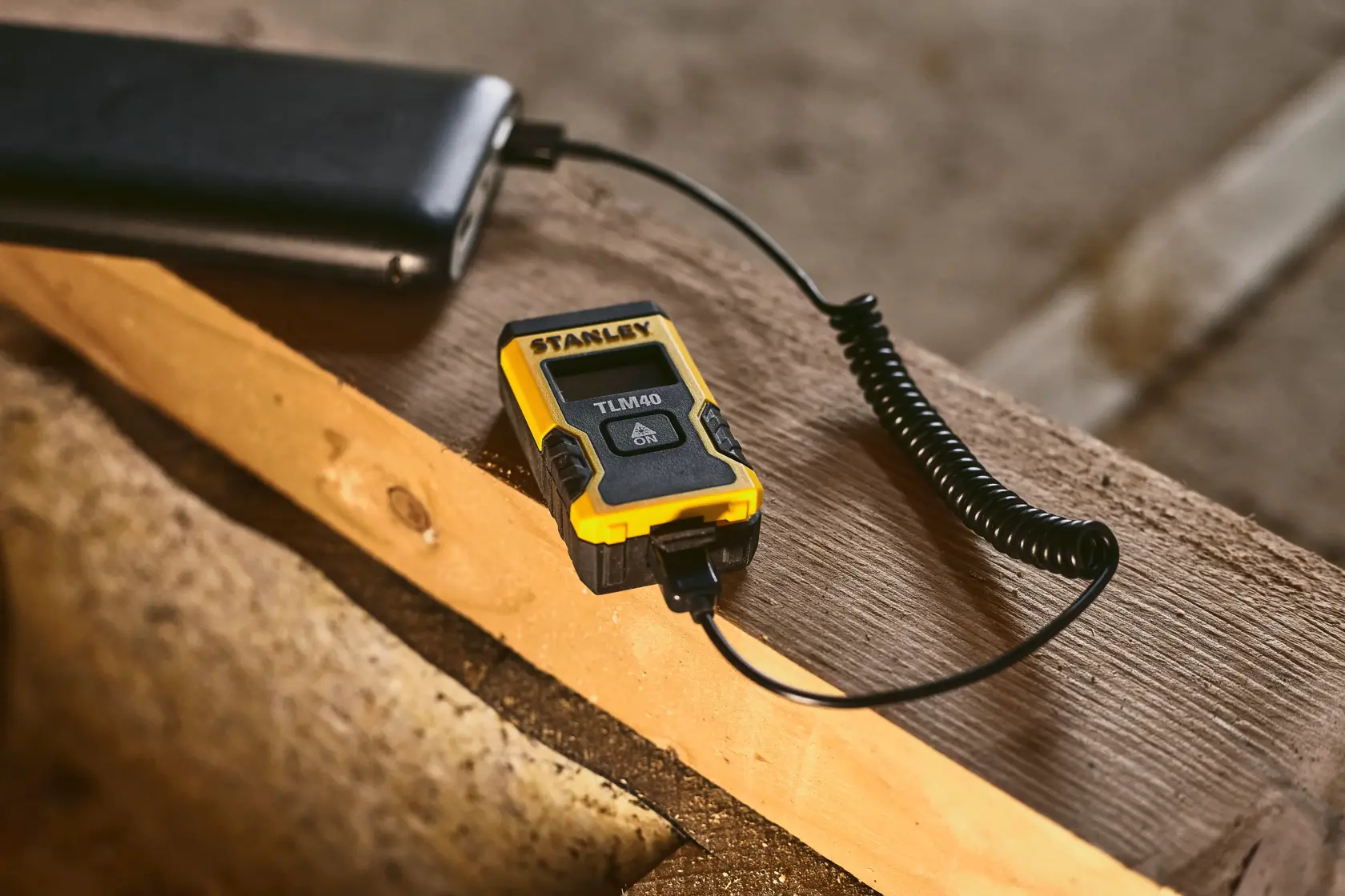 STANLEY STHT77666-0 Laser-Entfernungsmesser wird über USB-Kabel auf Holzoberfläche geladen.