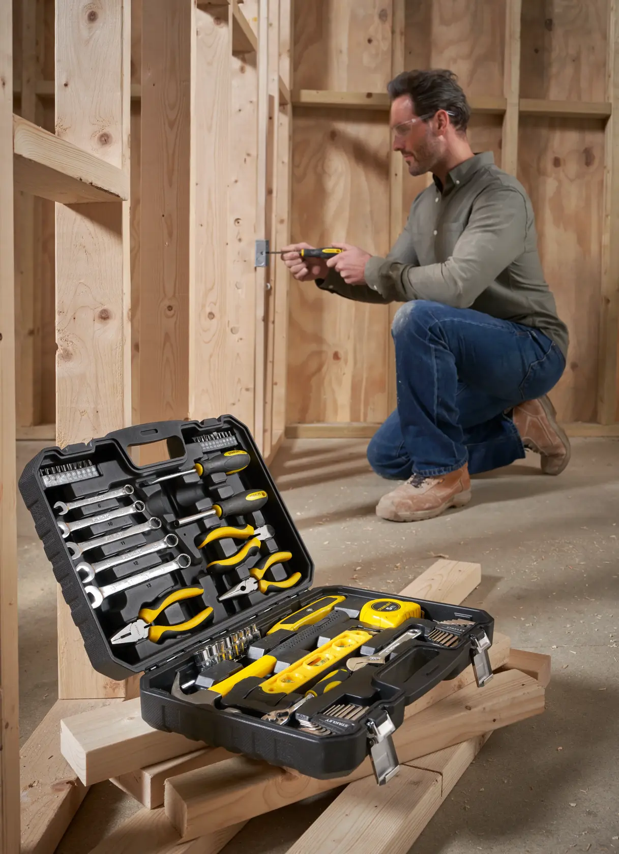 STANLEY STHT78050-1 tool kit case with assorted hand tools, shown open on wooden planks at a construction site.