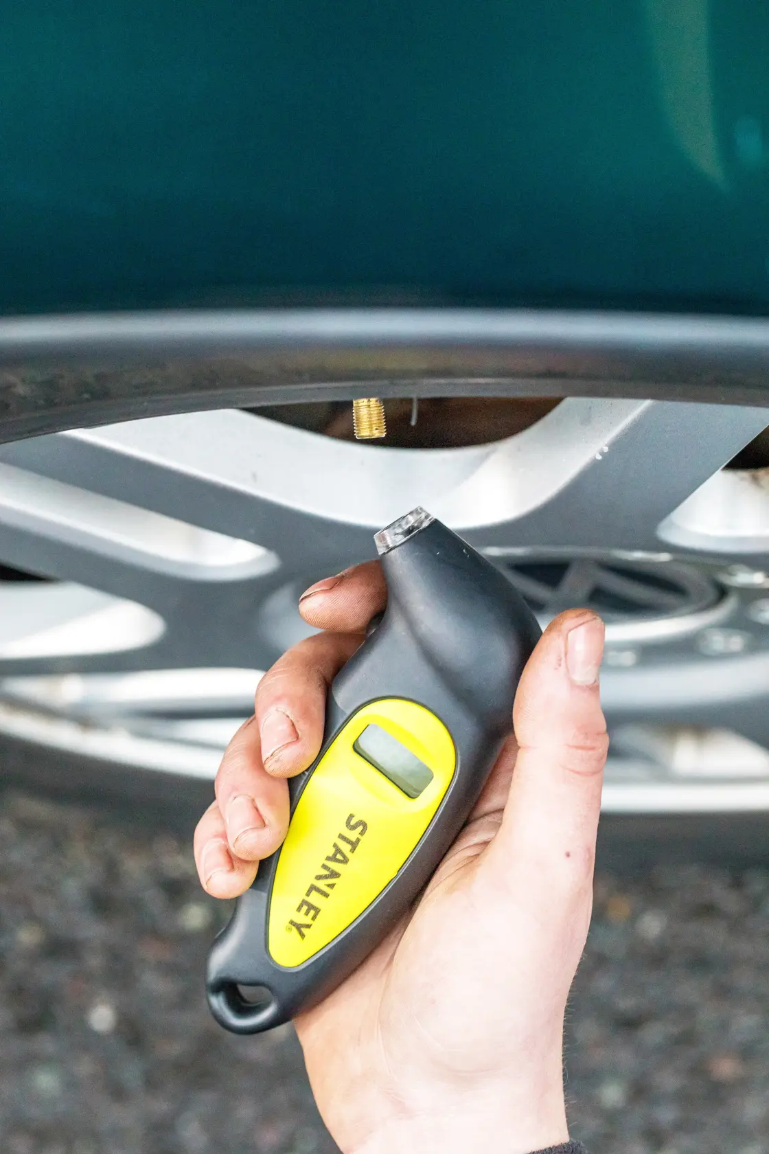 STANLEY STHT80874-0 digital tire pressure gauge held near a car wheel valve.