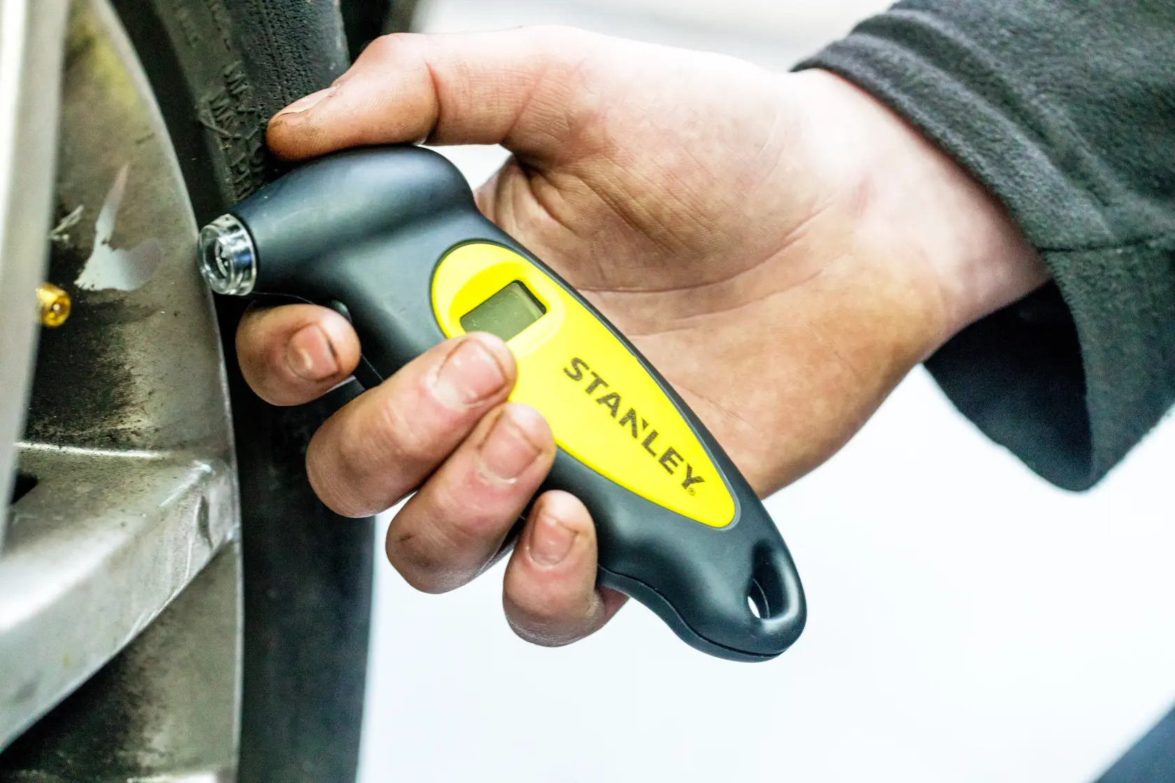 STANLEY STHT80874-0 tire pressure gauge held by hand next to car wheel.