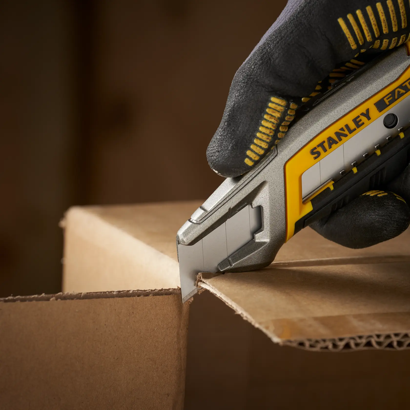 Photo of STANLEY STHT9-11301 utility knife cutting cardboard, held by gloved hand, close-up view.