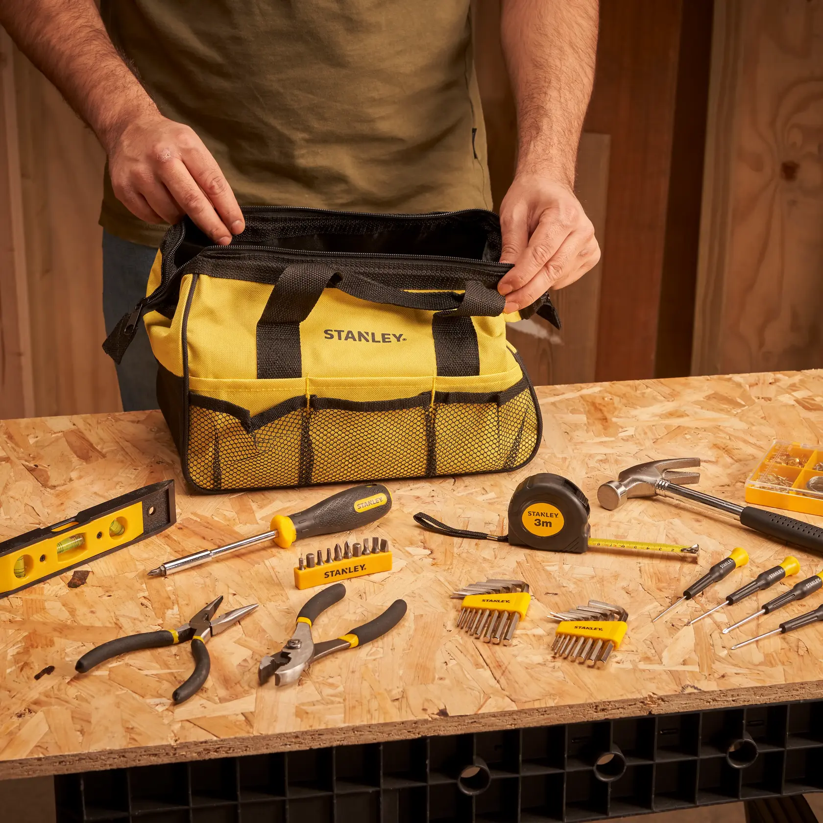 STANLEY STMT0-74101 tool bag with assorted tools on workbench, yellow and black, indoor workshop scene.
