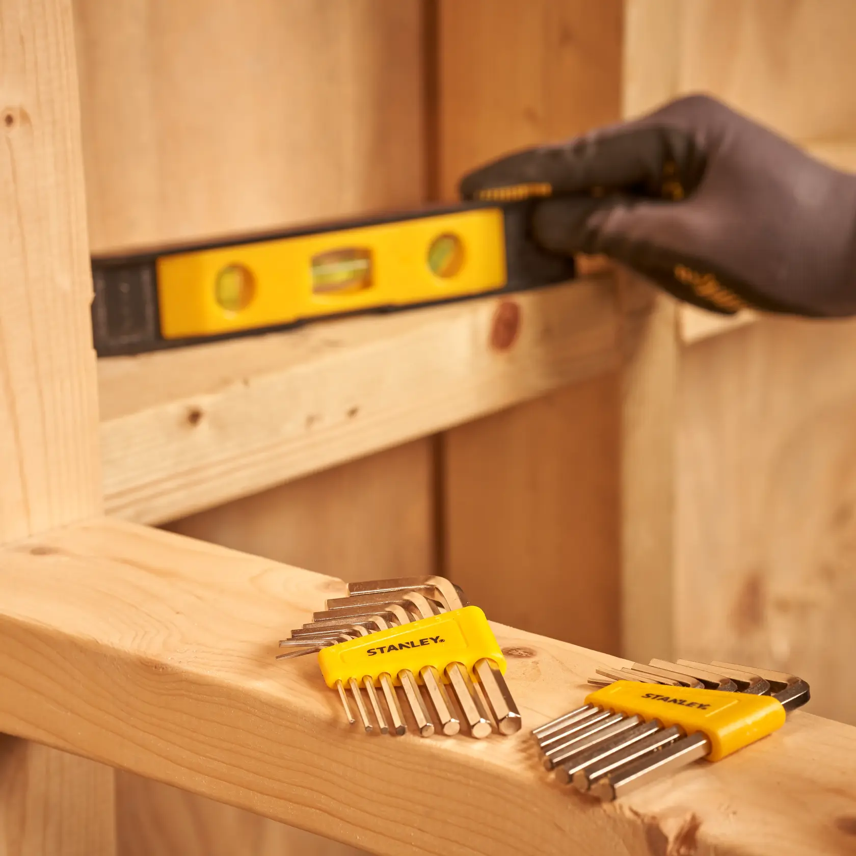 STANLEY STMT0-74101 hex key set on wood surface, person uses level tool in background, workshop scene.